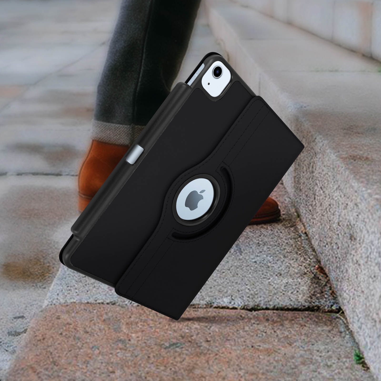 iPad nero in custodia nera, gambe di una persona e scarpe marroni sullo sfondo, su gradini di pietra.