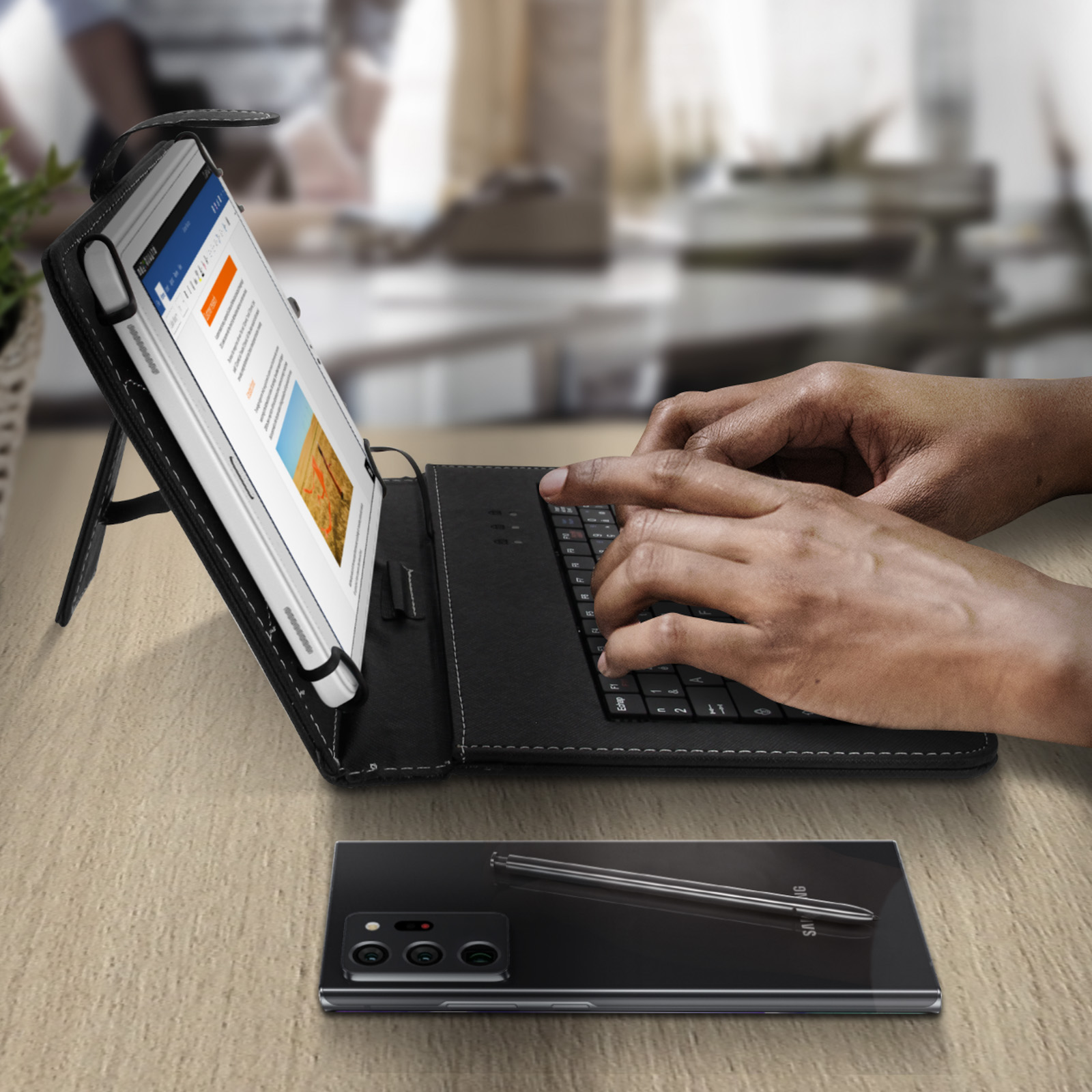 Una tableta en una funda negra con teclado está sobre una mesa de madera. Un teléfono y un bolígrafo debajo.