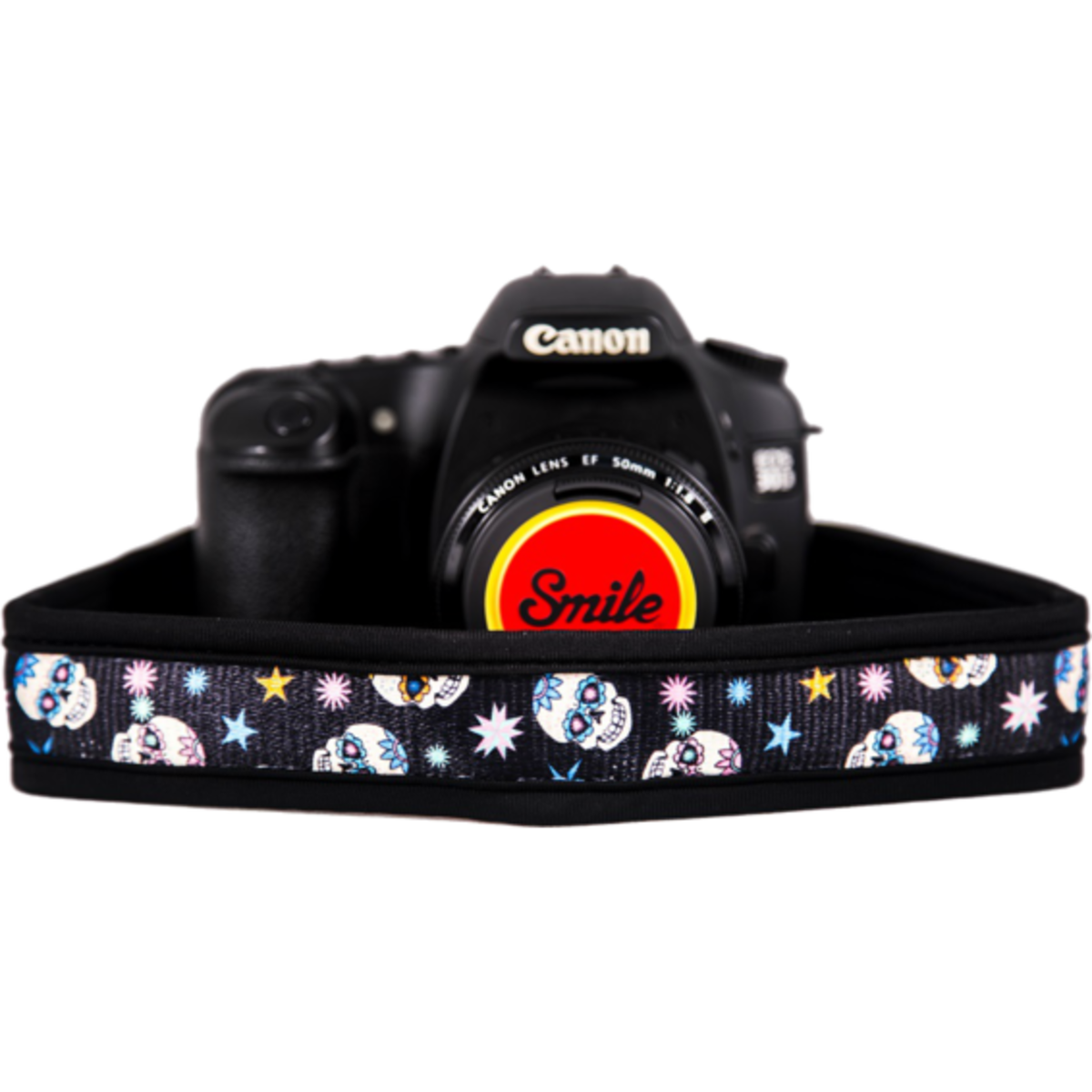 Cámara negra con correa colorida. La correa tiene diseños de calaveras y estrellas. Es visible una tapa de lente.
