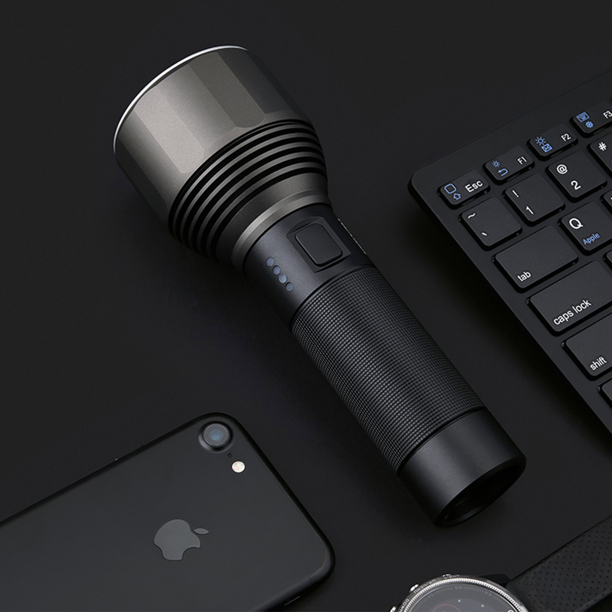 Linterna oscura con cuerpo negro y cabeza plateada. Fondo negro, con teléfono y reloj.