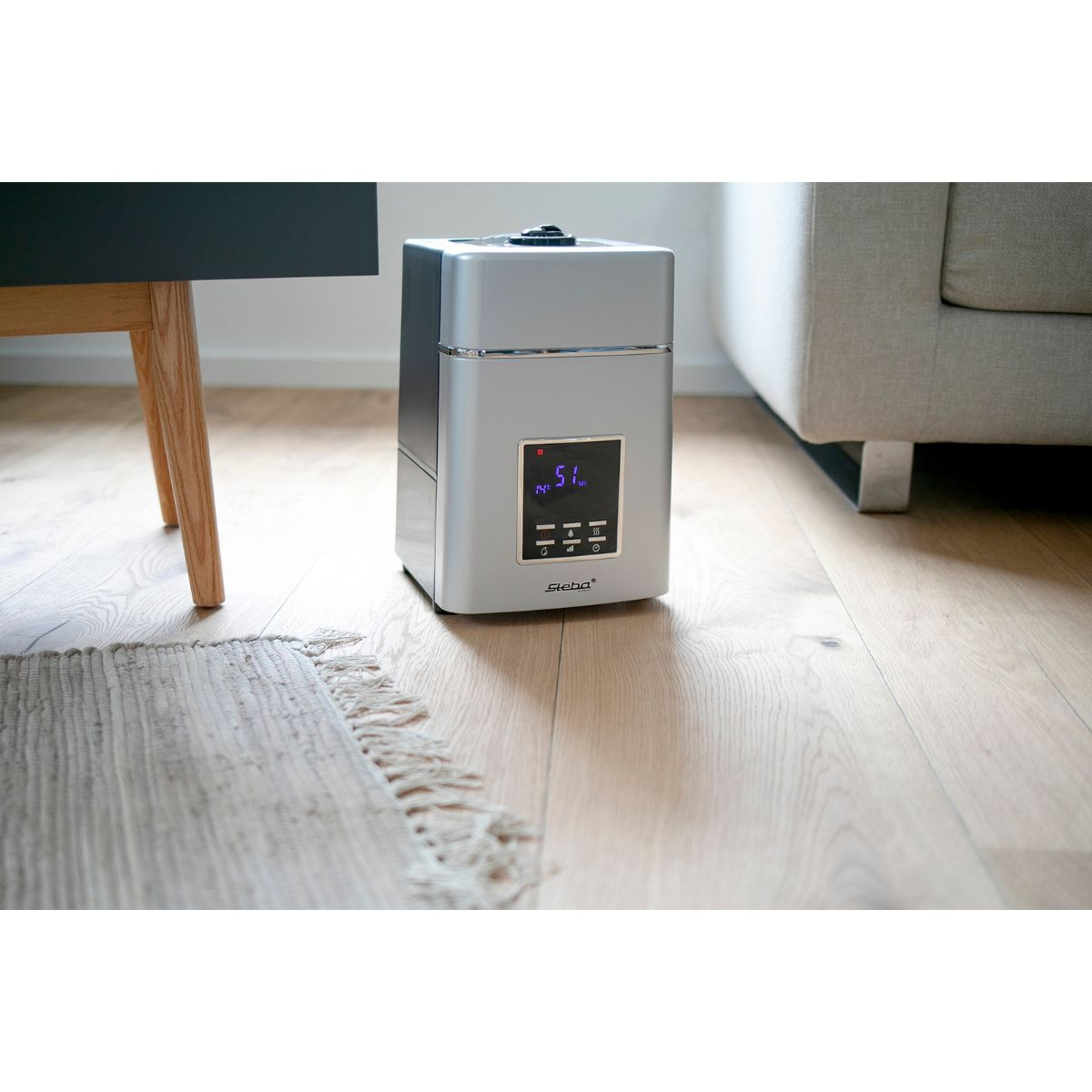 Umidificatore bianco e argento su pavimento in legno, vicino a tappeto e mobili. Sfondo bianco.