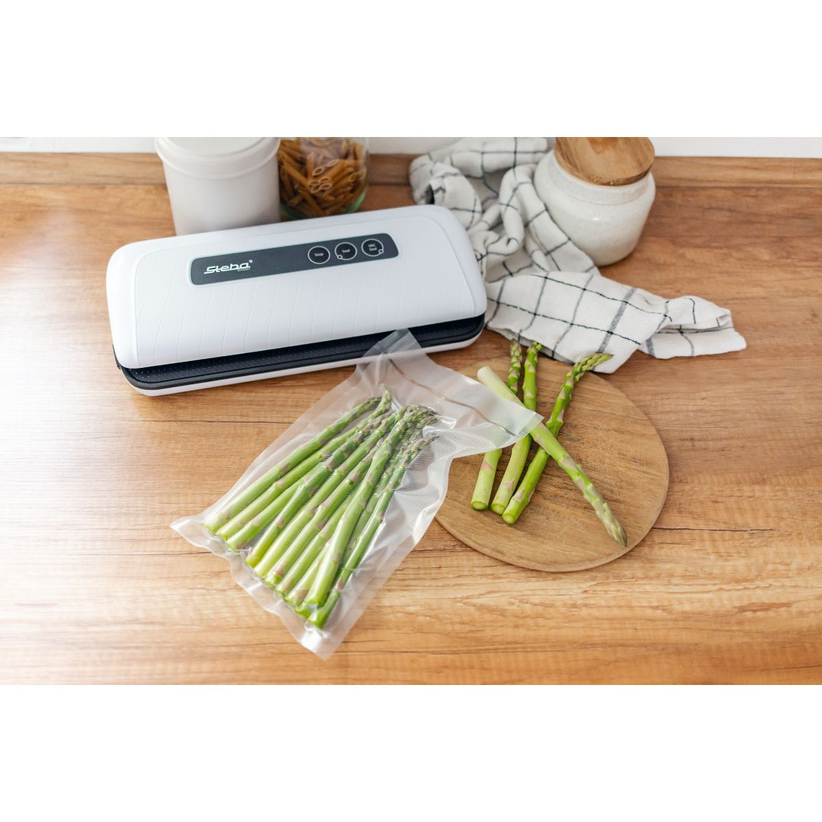 Vakuumiergerät mit Spargel und Utensilien auf einem Holztisch.
