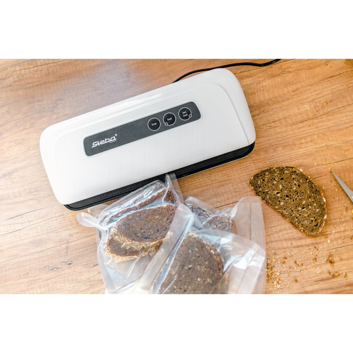 Weißer Vakuumierer mit Brotscheiben in Plastiktüte auf Holztisch.