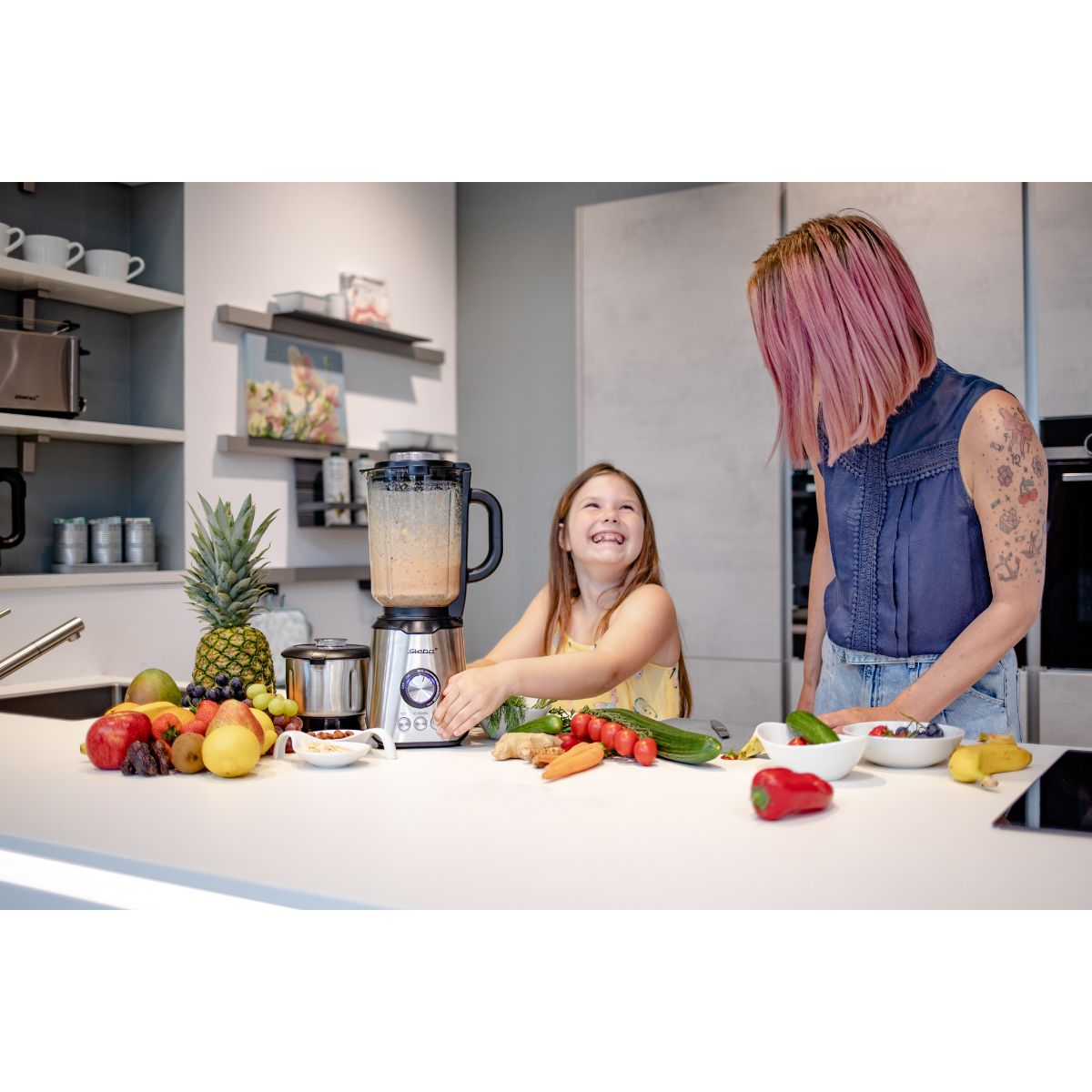 Ein Mixer mit Zutaten und zwei Frauen, die gemeinsam einen Smoothie zubereiten.