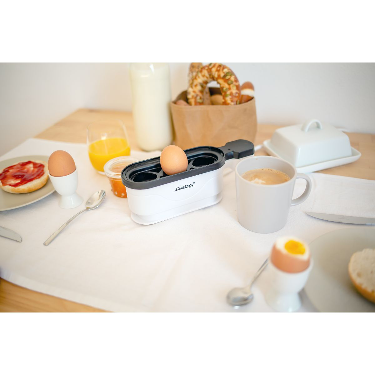 Śniadanie z jajkami na twardo, sokiem pomarańczowym, chlebem i białą maszynką do gotowania jajek.