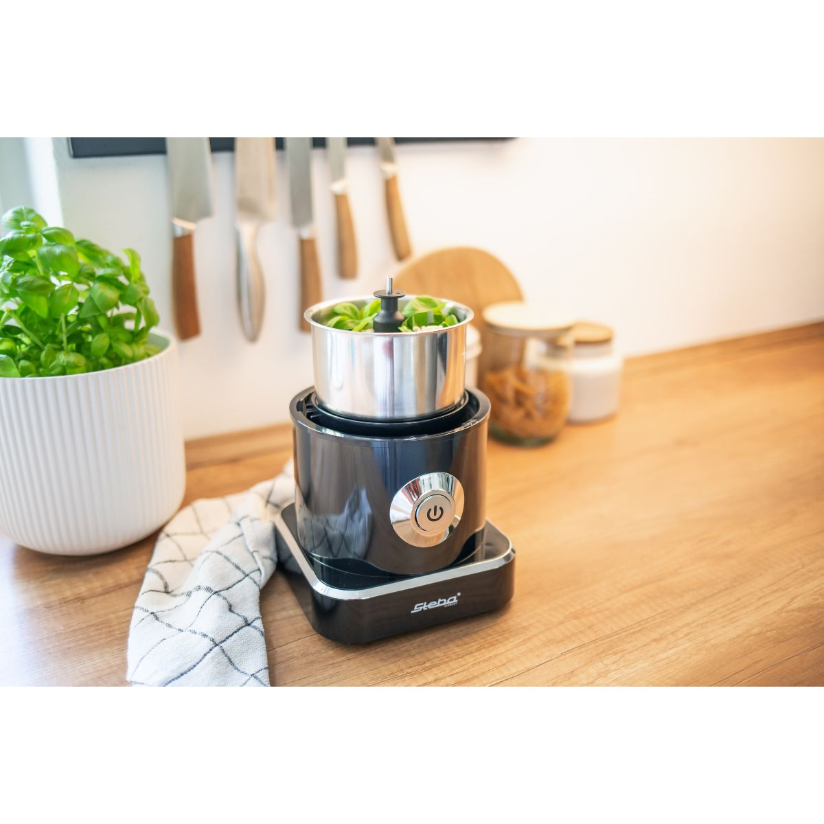Un robot da cucina nero con una ciotola in acciaio inox, su una superficie di legno.