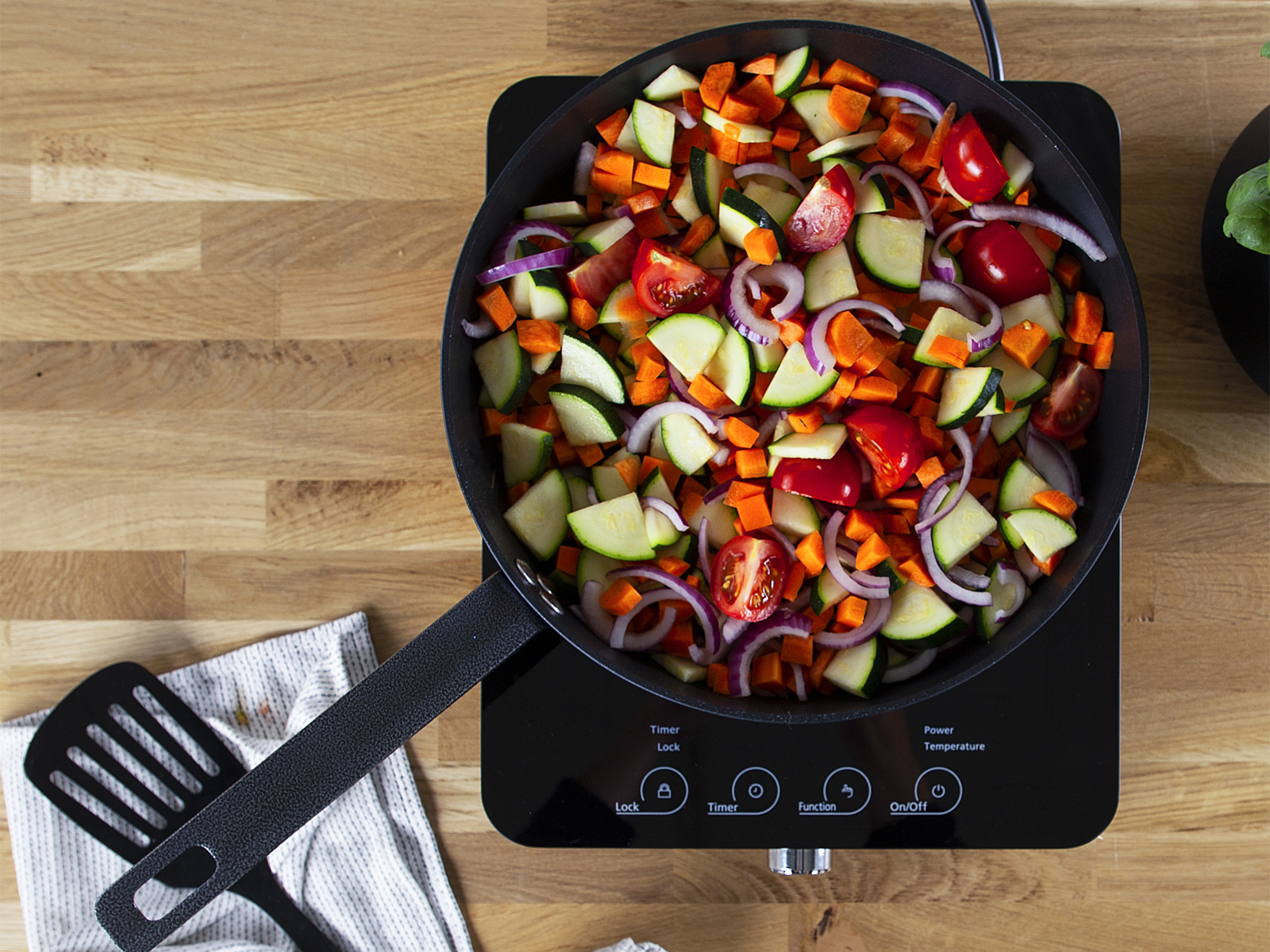 Warzywa na patelni na czarnej płycie indukcyjnej, drewniana powierzchnia.