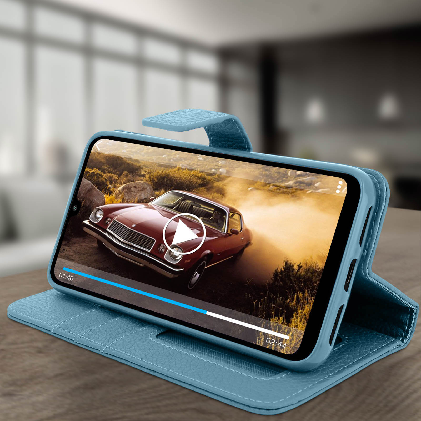 Telefono in custodia blu, mostra video di auto. Tavolo di legno, sfondo sfocato.