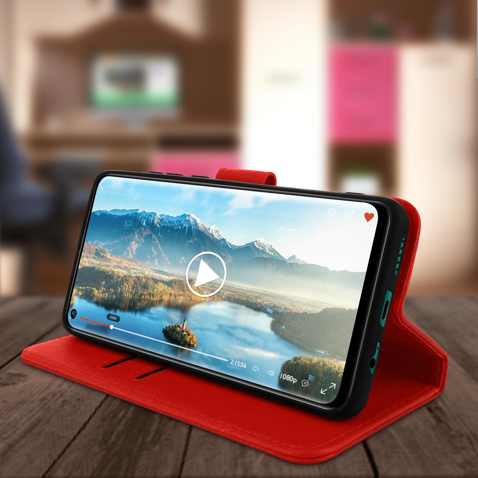 Smartphone in custodia rossa mostra un video su un tavolo di legno.