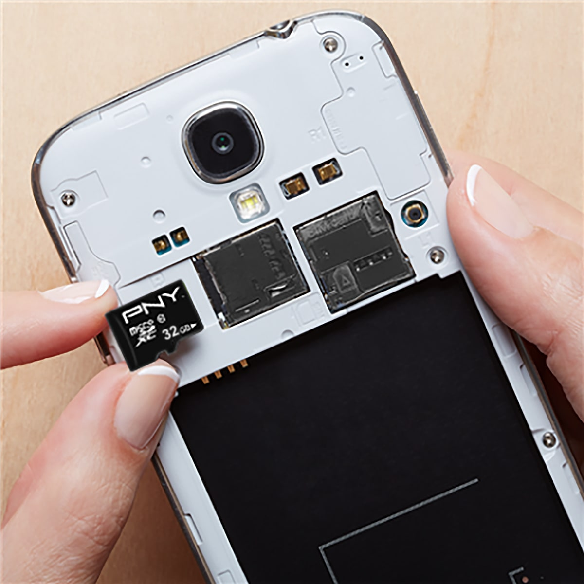 Dłoń wkładająca kartę micro SD PNY 32GB do telefonu, na drewnianej powierzchni.