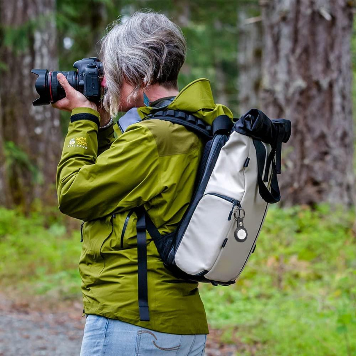 Eine Frau in einer grünen Jacke, die mit einer Kamera fotografiert. Ein Rucksack ist auf dem Rücken. Bäume sind im Hintergrund.