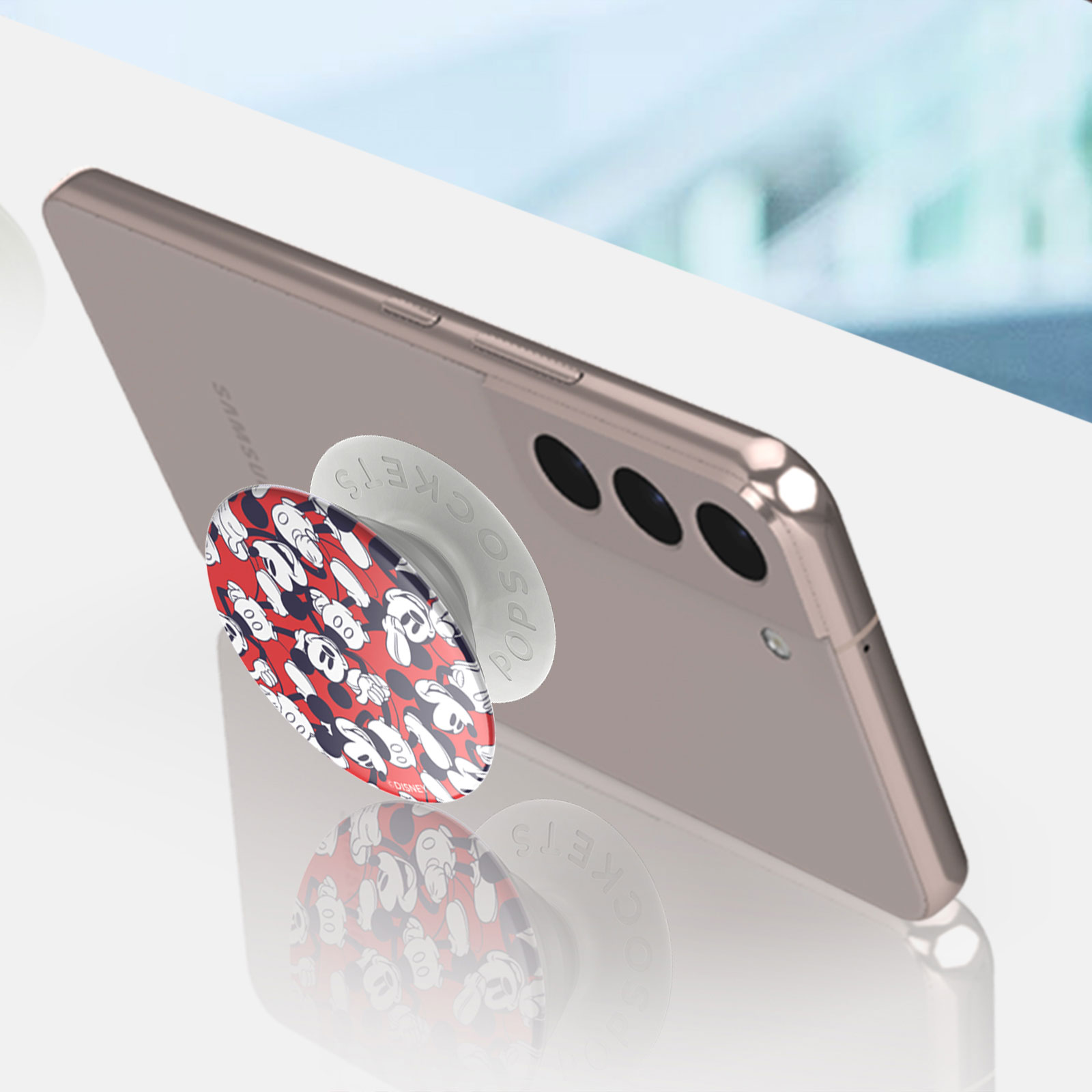 Telefon mit einem Mickey Mouse PopSocket. Er liegt auf einer weißen Oberfläche.