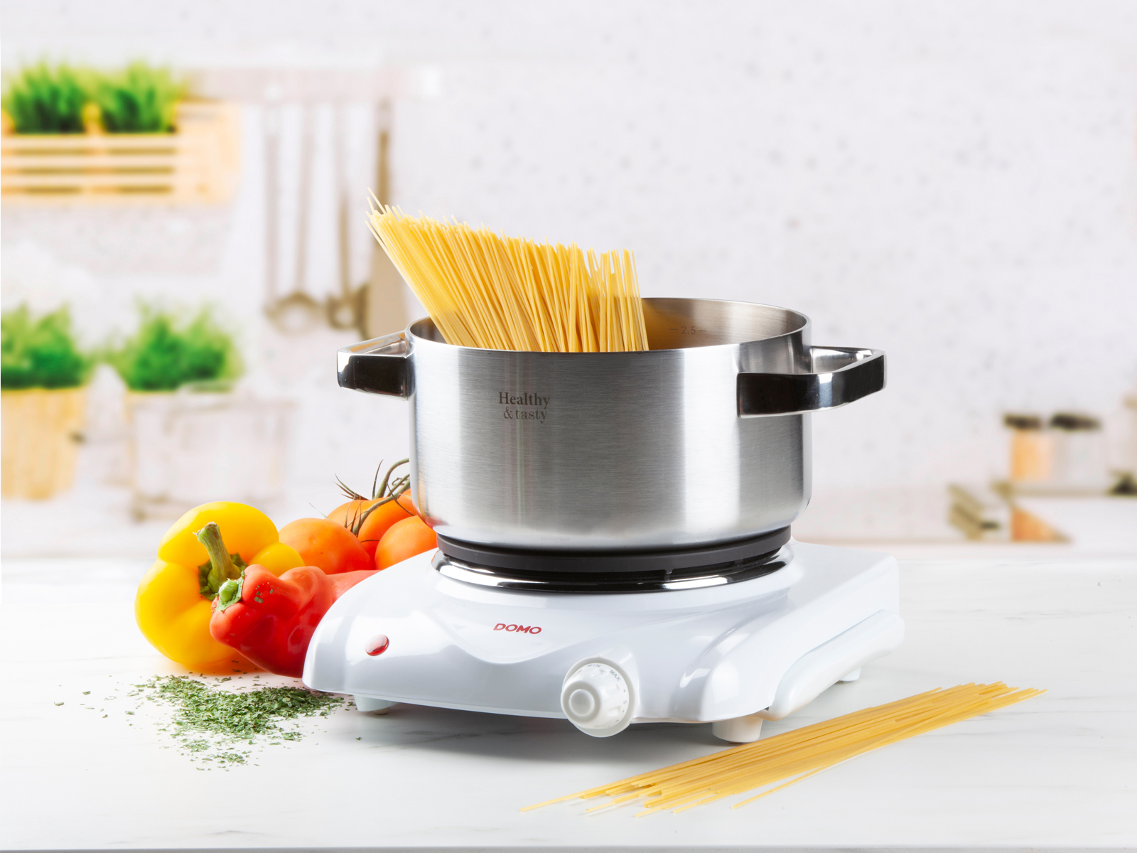 Topf mit Spaghetti auf einem weißen Elektroherd, Tomaten, Paprika und Kräutern.