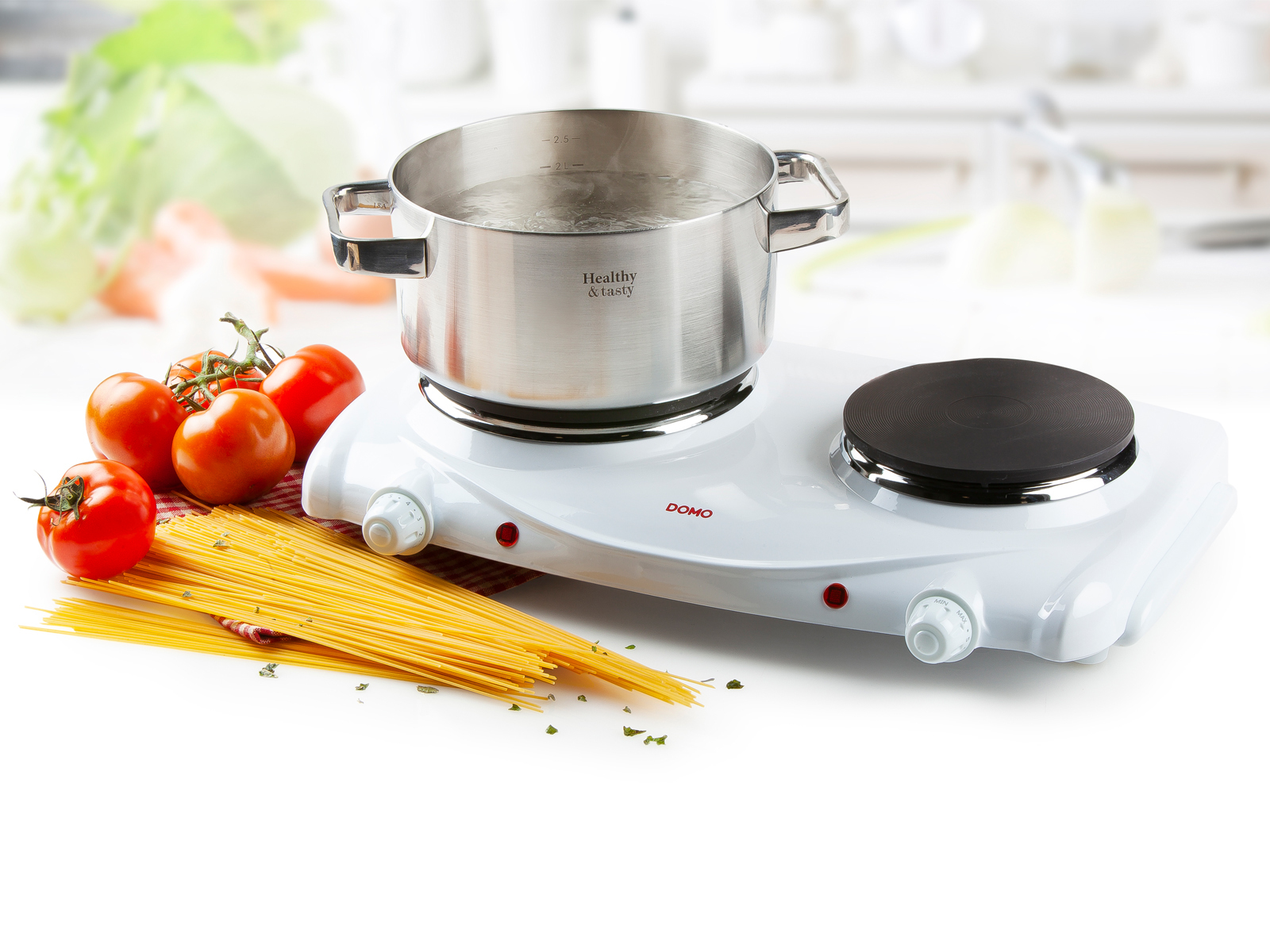 Garnek wrzącej wody na białej kuchence, z pomidorami i makaronem z boku, w kuchni.