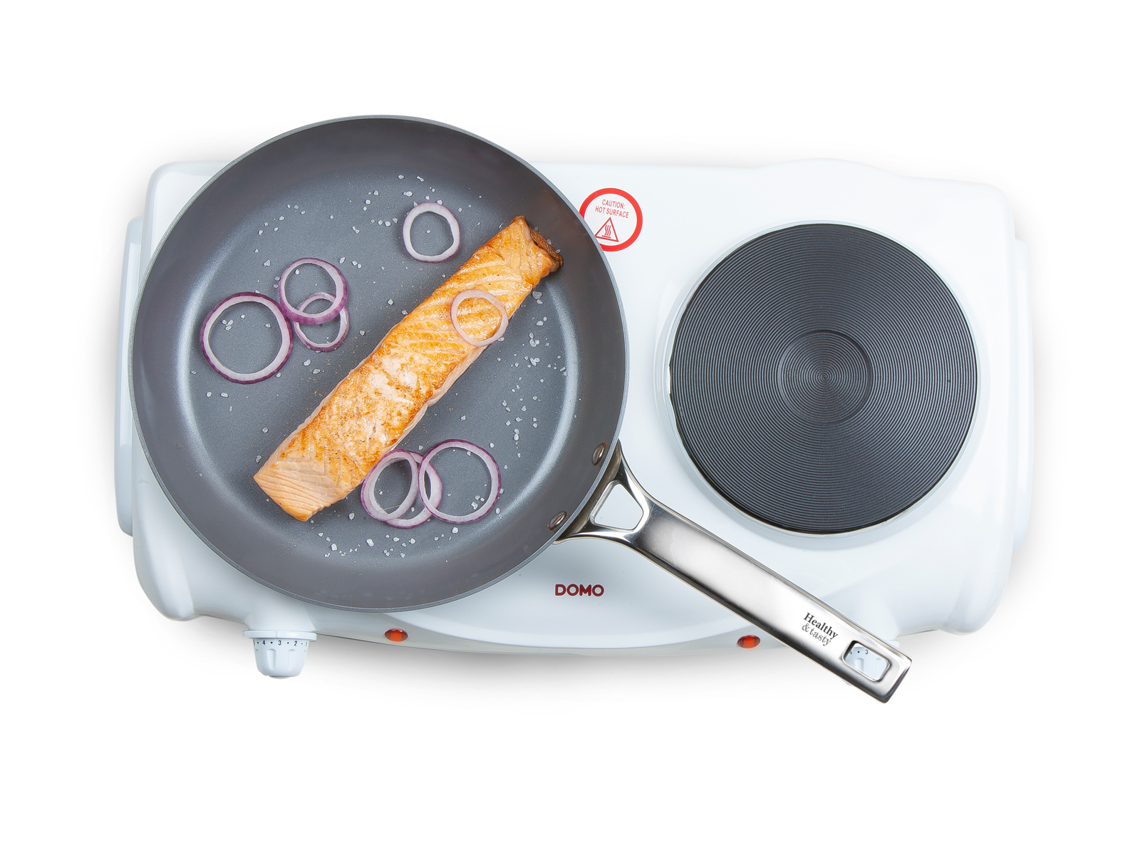 Widok z góry na patelnię z łososiem, cebulą i solą. Na białej podwójnej płycie grzewczej.