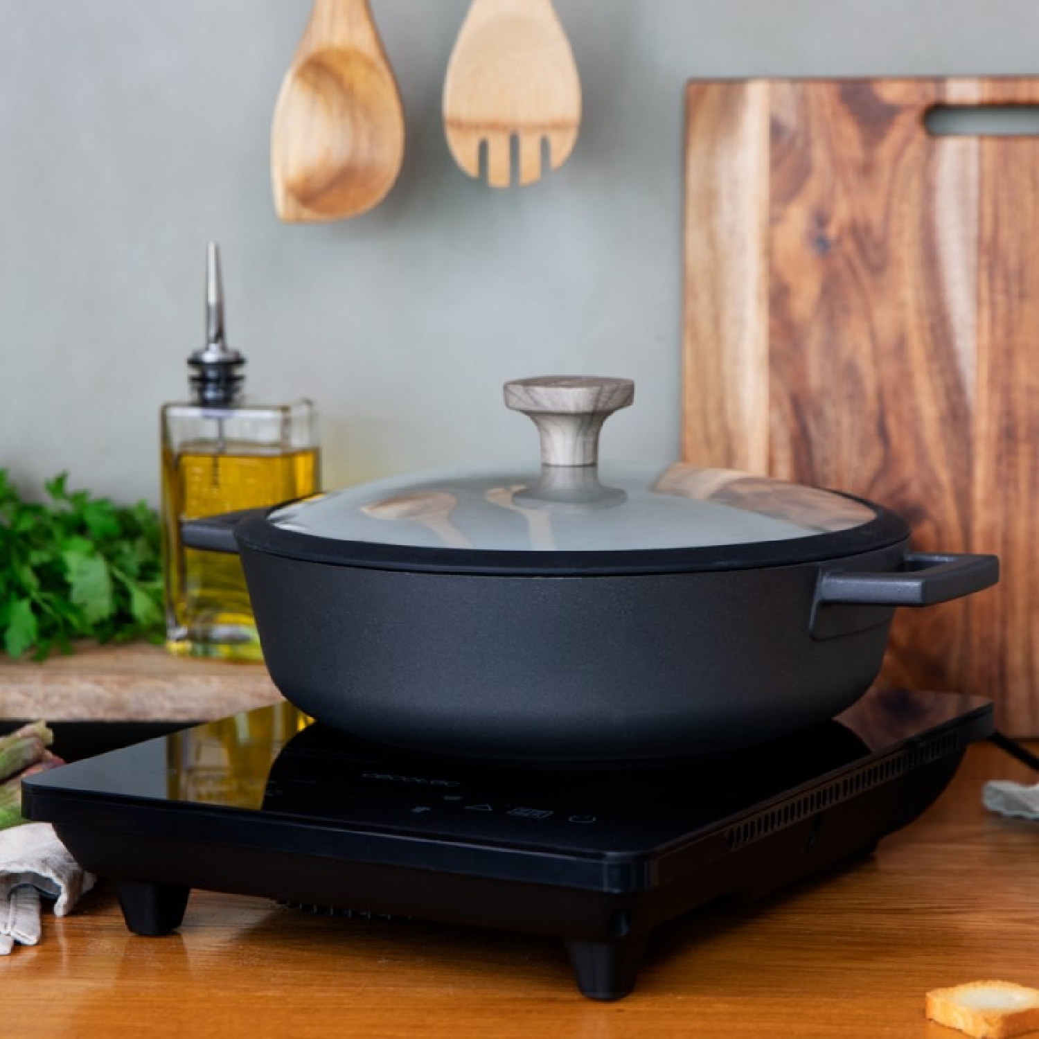 Czarny garnek na płycie indukcyjnej z drewnianymi przyborami i deską.