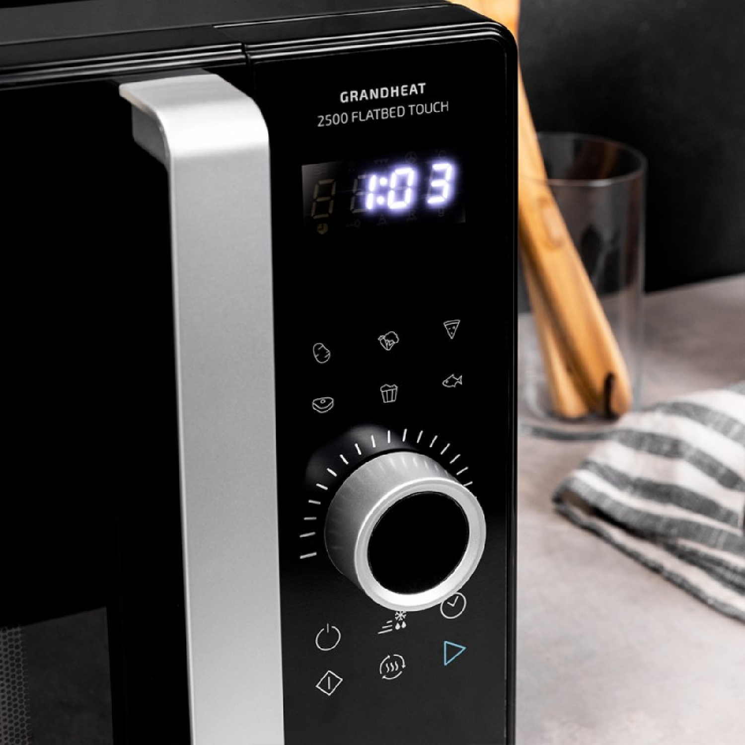 Czarny panel sterowania kuchenki mikrofalowej. Wyświetlacz pokazuje czas, z pokrętłami i przyciskami do ustawień.