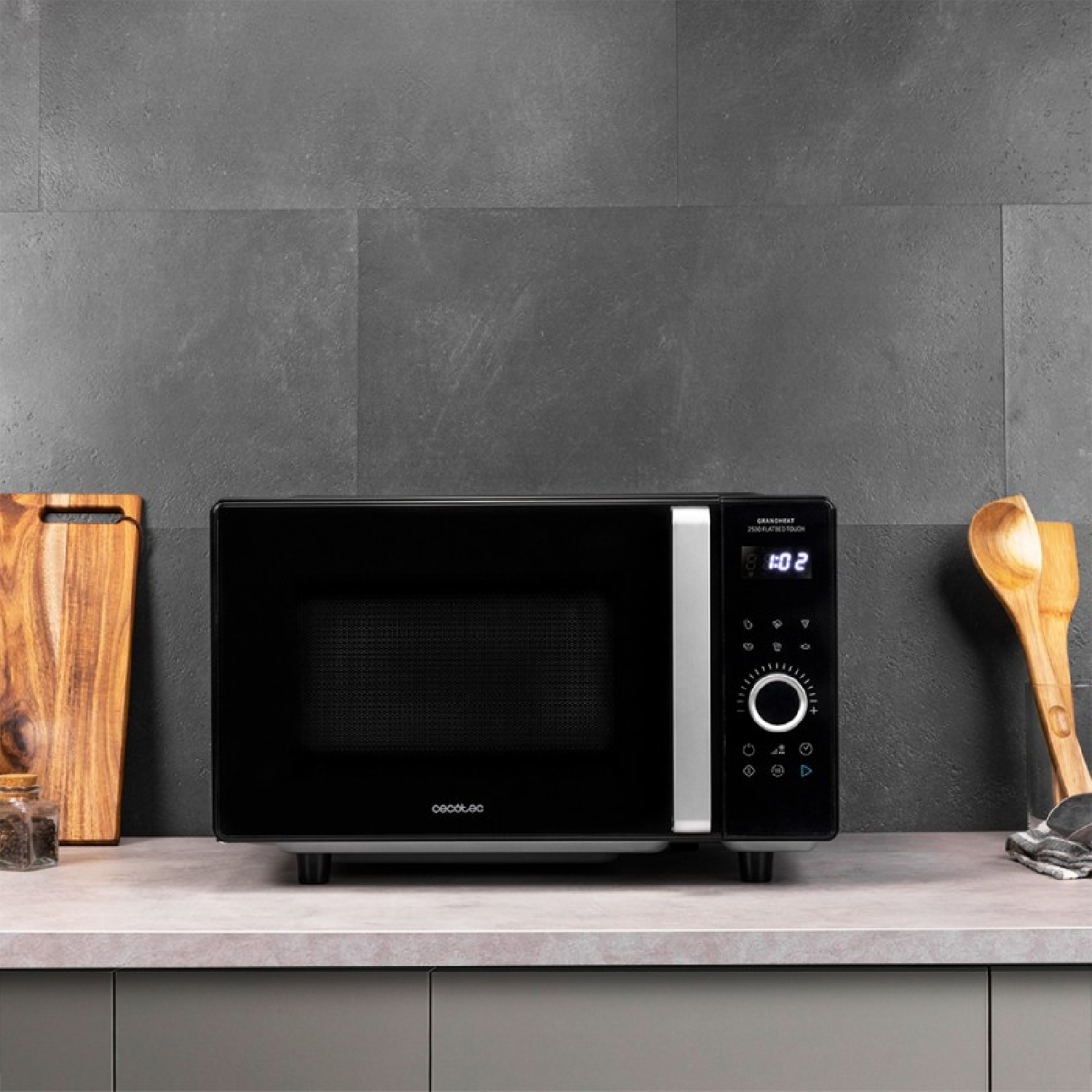 Czarna kuchenka mikrofalowa na szarym blacie z drewnianą deską do krojenia i przyborami kuchennymi w pobliżu.