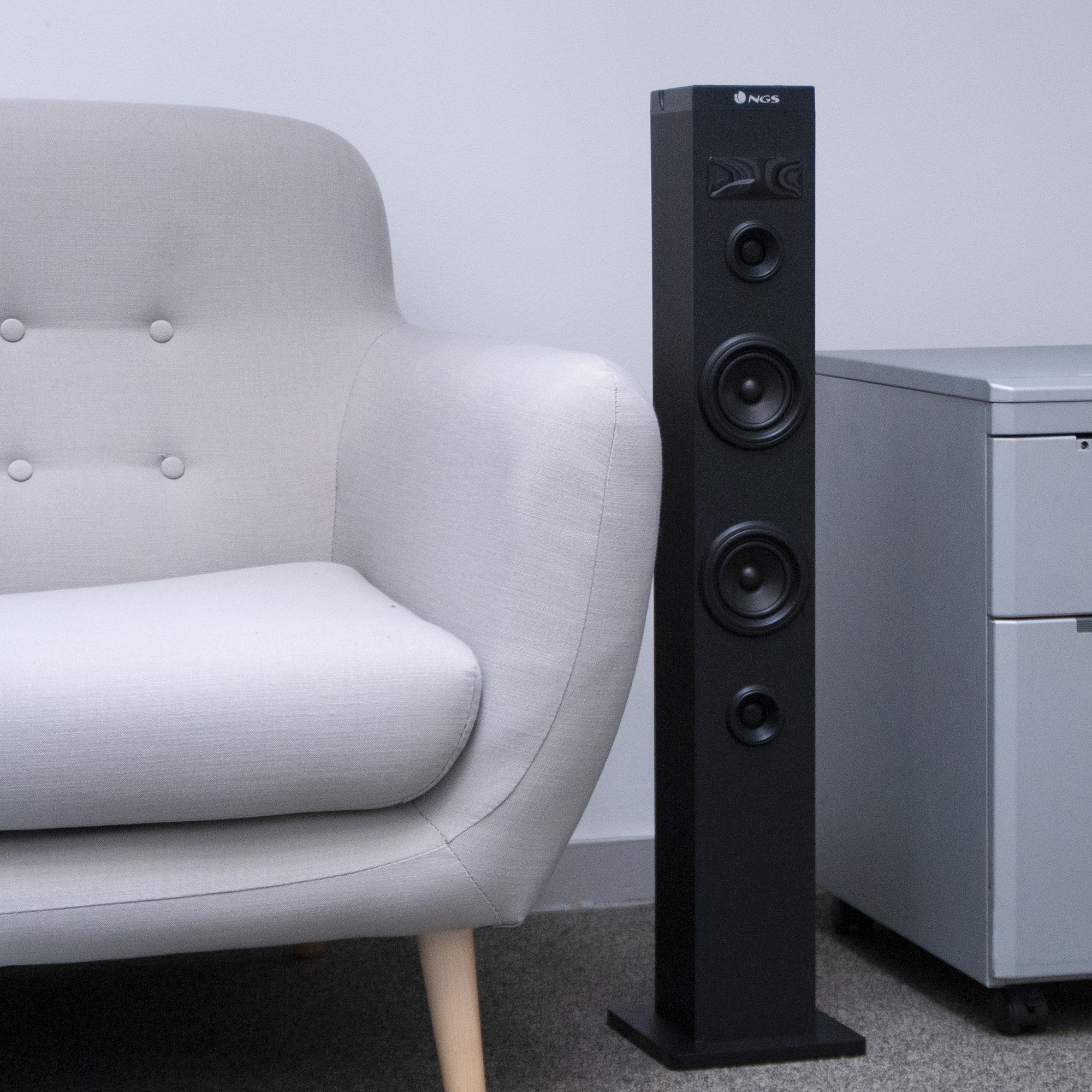 Altavoz negro alto junto a un sillón y armario grises.  La marca NGS está impresa.