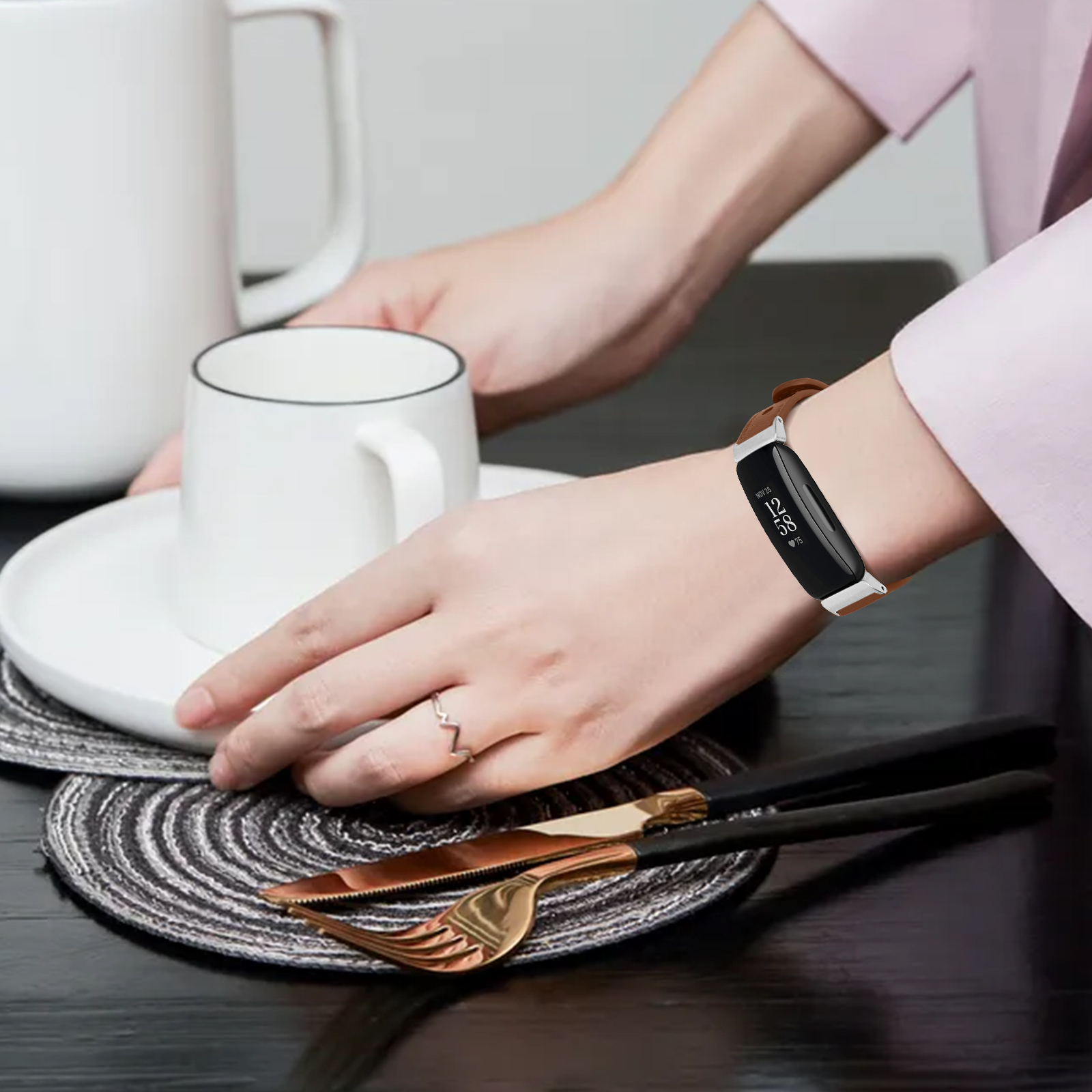 Hand mit Smart-Armband, Teller mit Tasse, Messer und Gabel auf dem Tisch.