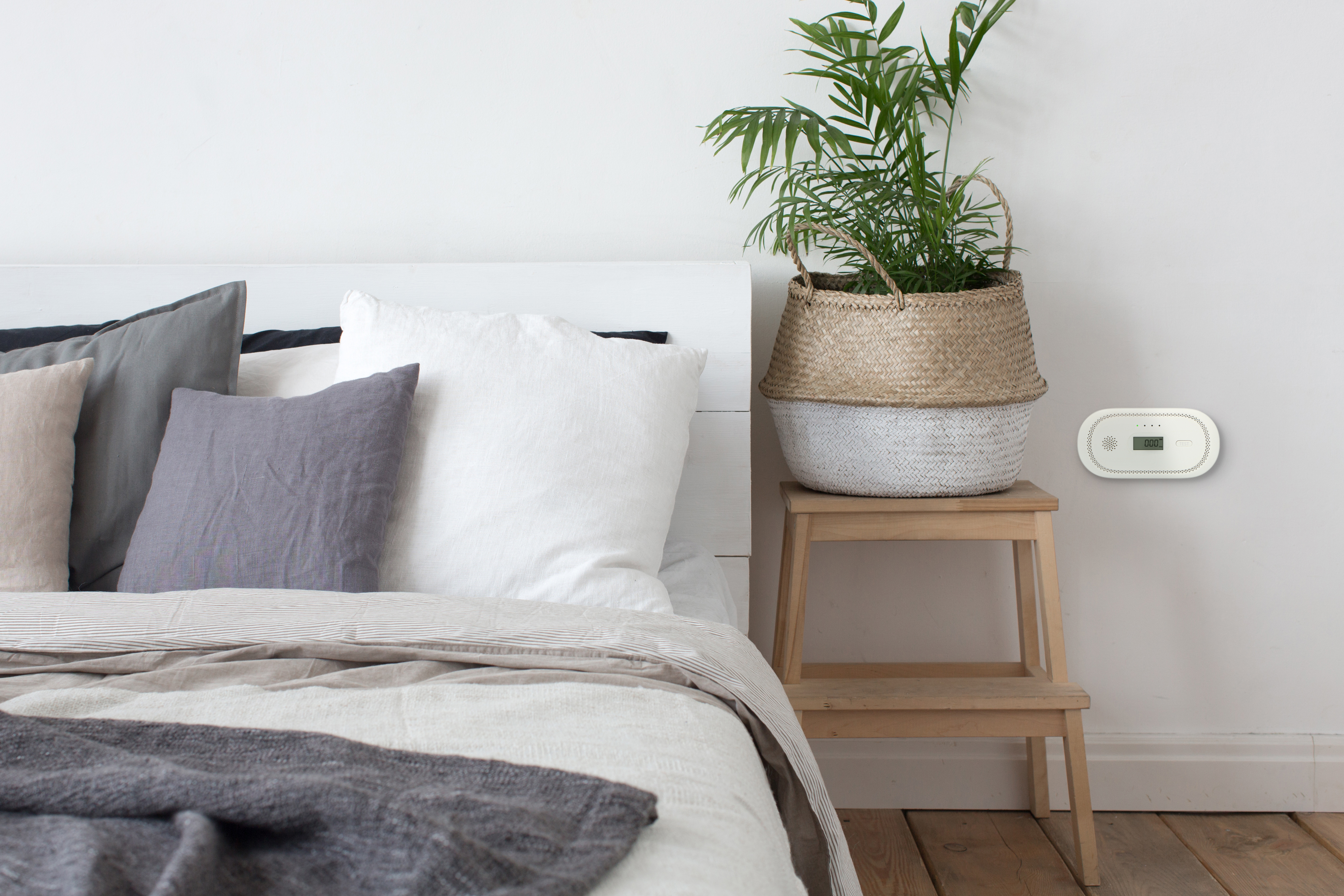 Schlafzimmer. Bett mit Kissen, Pflanze auf Hocker und Wandgerät.