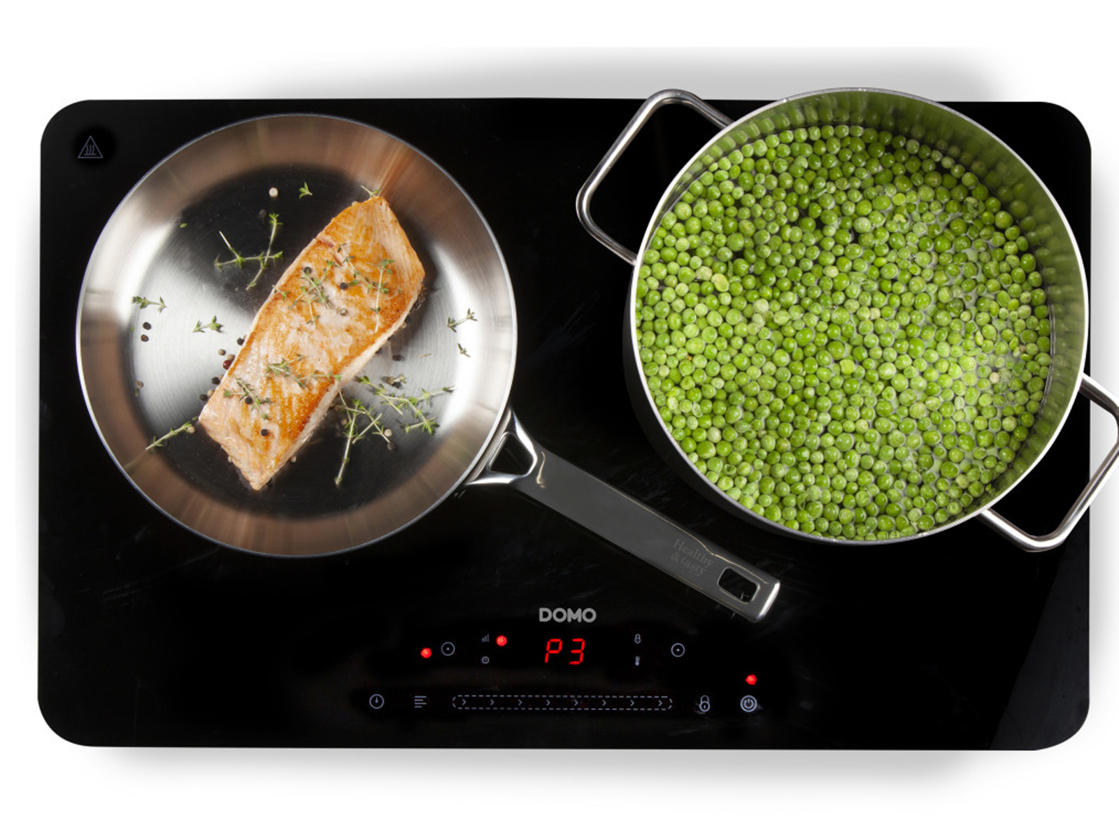 Plaque de cuisson avec une poêle de saumon et une casserole de petits pois.