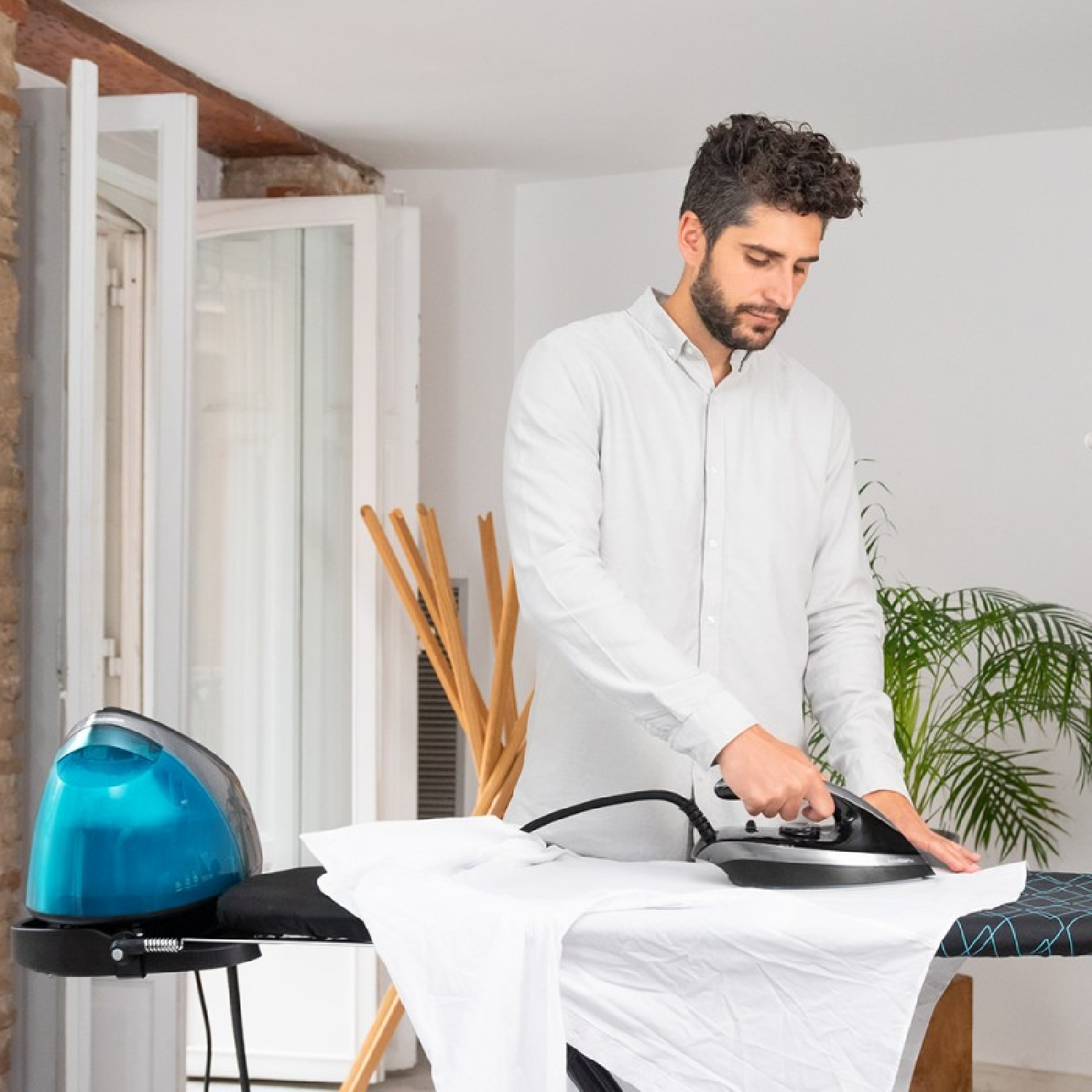 Hombre planchando una camisa blanca en una tabla de planchar. Plancha azul y negra.