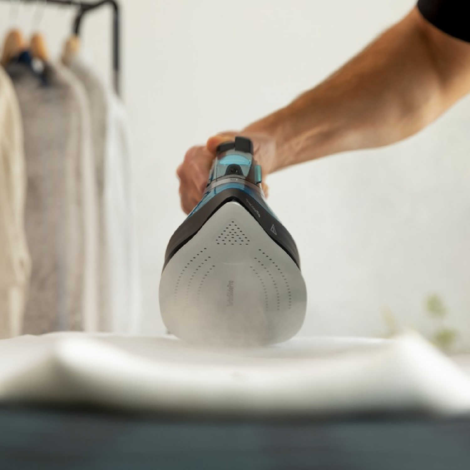 Ręka osoby trzyma żelazko parowe nad białym materiałem. Widoczna para.