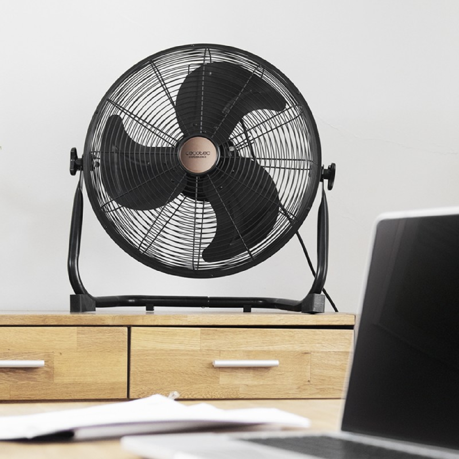 Ventilador negro sobre un escritorio de madera. El ventilador apunta lejos del espectador.