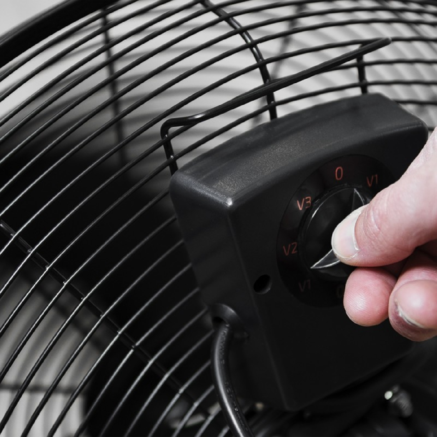 Primer plano de un ventilador con una mano ajustando el dial de velocidad. Ventilador negro, dial negro.