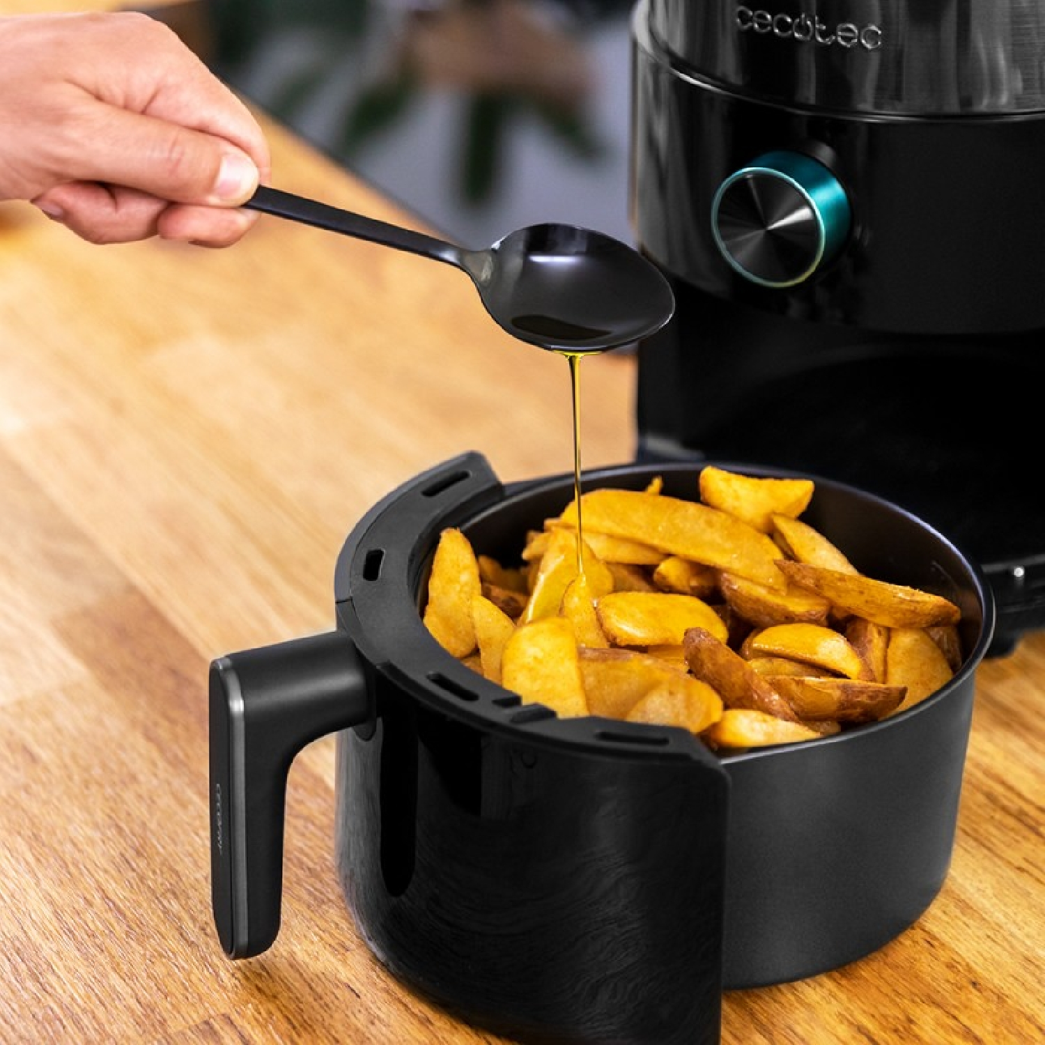 L'olio viene versato da un cucchiaio sulle patatine fritte in un cestello nero per friggitrice ad aria.