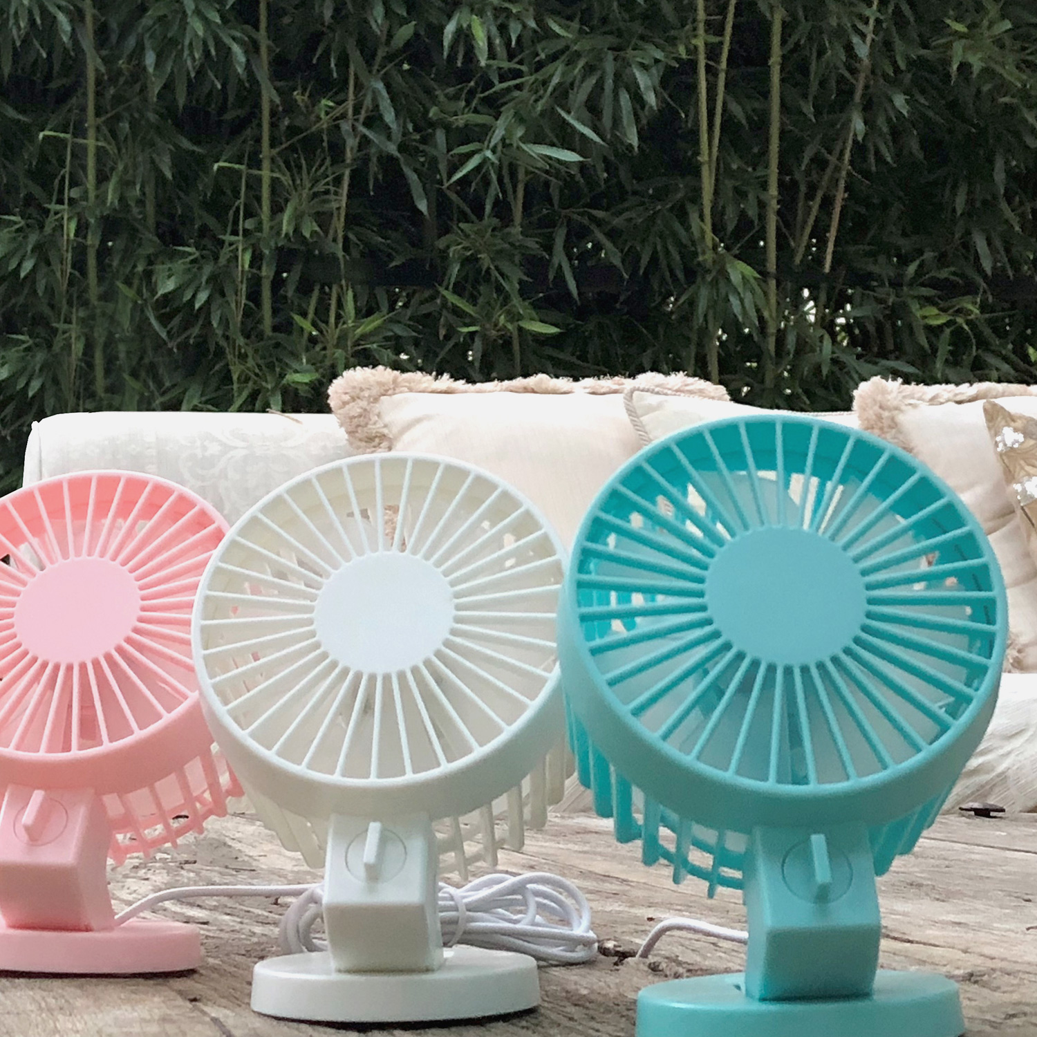 Tre piccoli ventilatori colorati su una superficie di legno. Bambù e un cuscino color crema sullo sfondo.