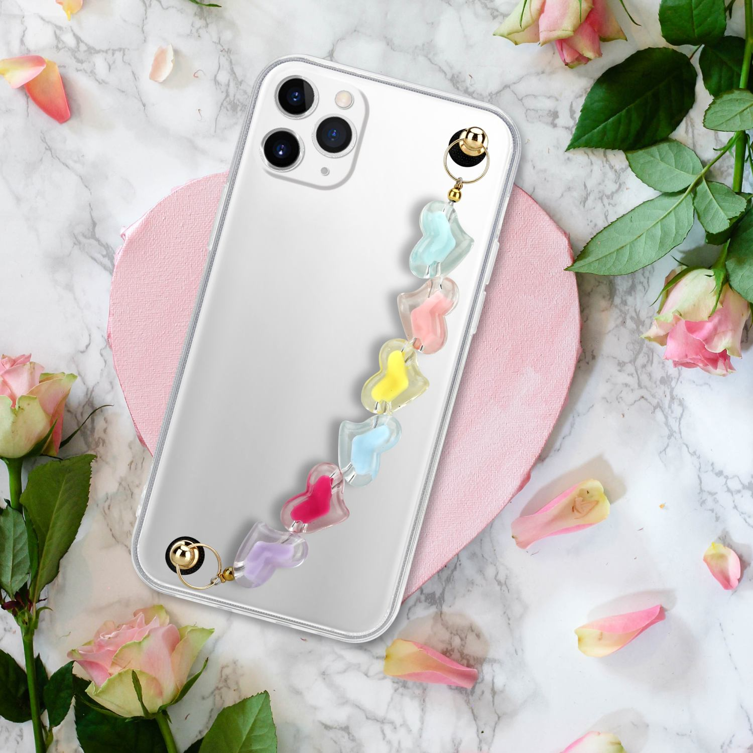 Ein Telefon mit einem Anhänger. Rosen im Hintergrund. Das Telefon liegt auf einer Marmoroberfläche.