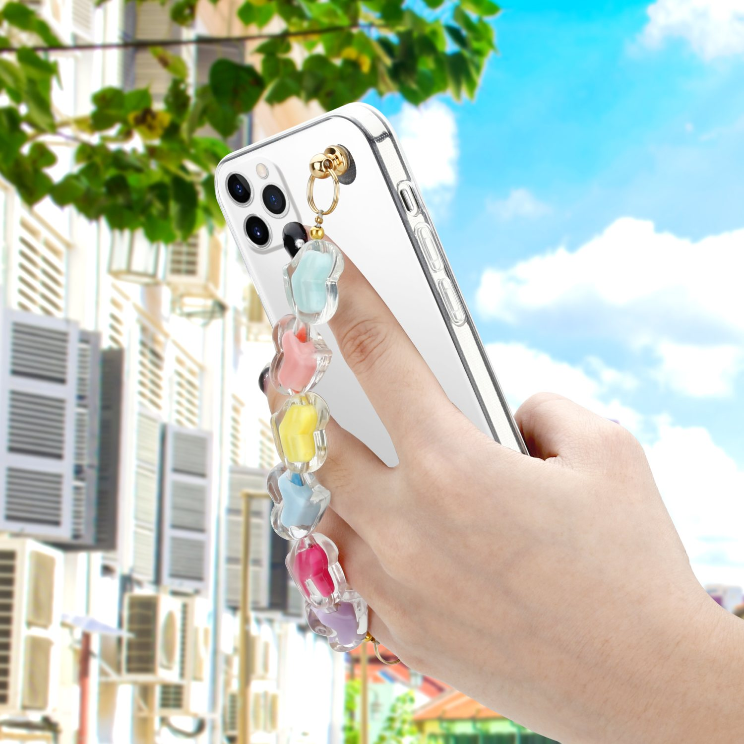 Hand hält ein Telefon mit bunter Kette. Hintergrund zeigt Gebäude und blauen Himmel.