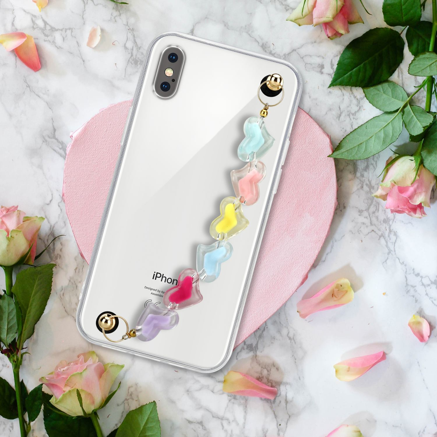 Transparente Handyhülle mit einem Telefon und einem Anhänger. Das Telefon liegt auf Marmor mit Blumen.