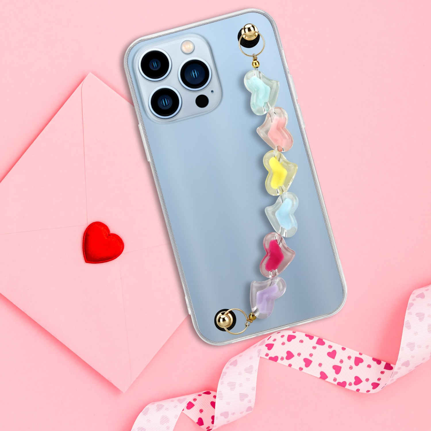 Telefon mit herzförmigem Anhänger. Ein rosa Umschlag mit rotem Herz liegt unter dem Telefon.