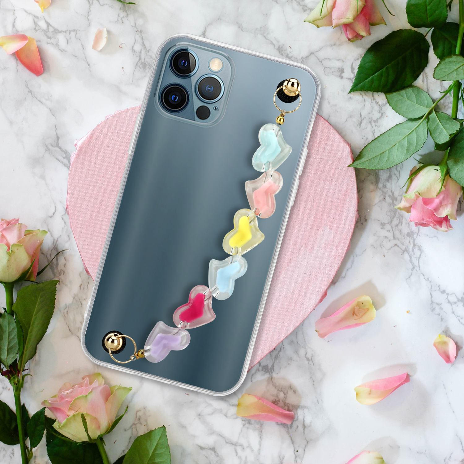 Telefon mit herzförmigem Riemen. Rosen, Blütenblätter auf Marmorhintergrund.