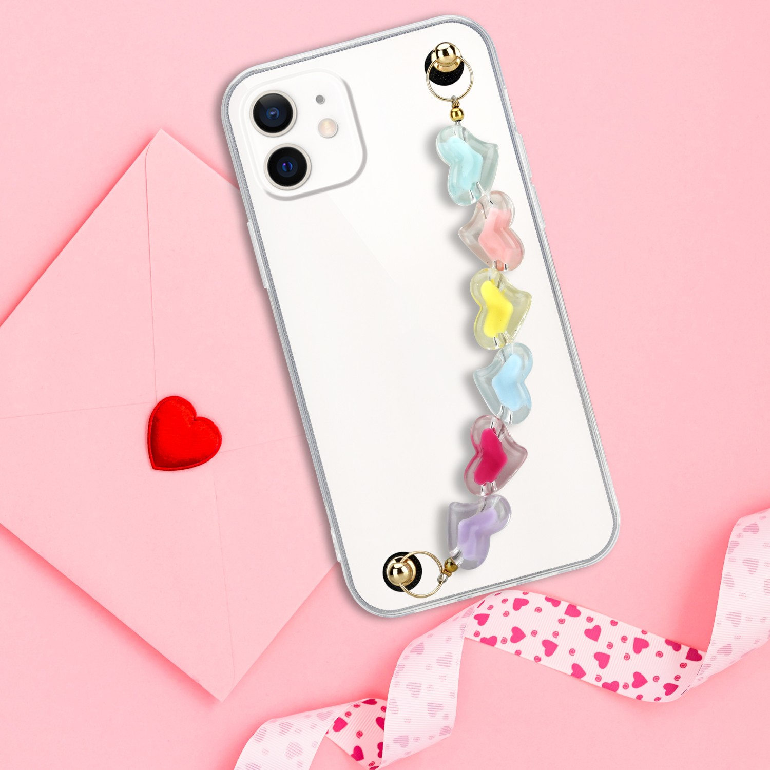 Ein weißes Telefon mit einem bunten herzförmigen Anhänger. Auf rosa Oberfläche mit Herz und Band platziert.