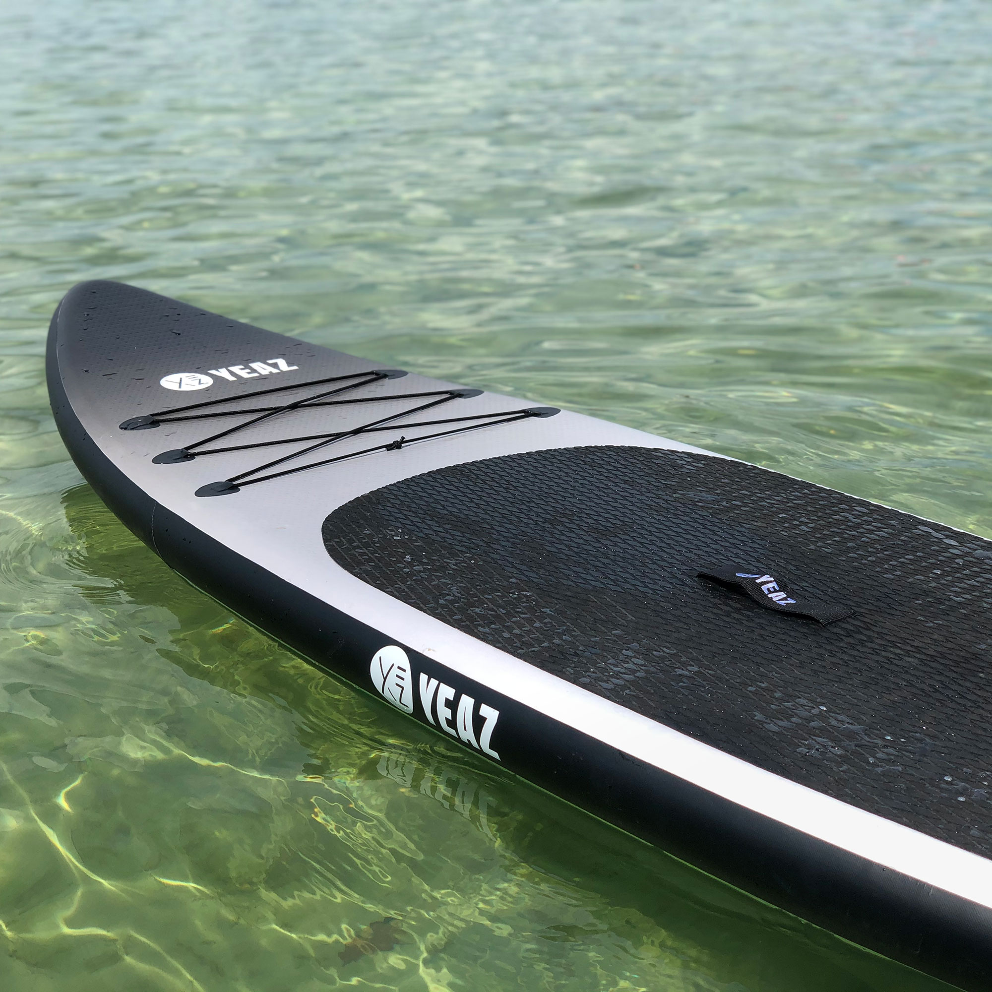 Stand-Up-Paddleboard in klarem Wasser. Schwarzes Paddleboard mit silbernen und schwarzen Details. Klares Wasser mit Lichtreflexion.