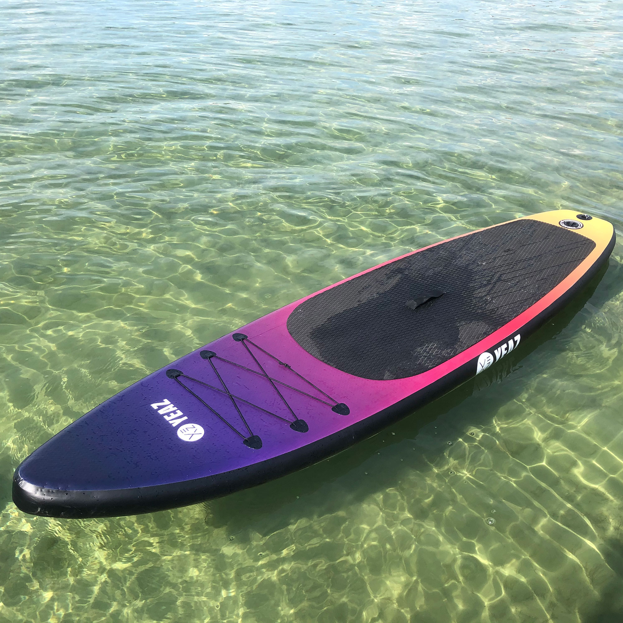 Ein farbenfrohes Paddleboard schwimmt in klarem Wasser. Das Board wechselt von lila zu pink zu gelb.