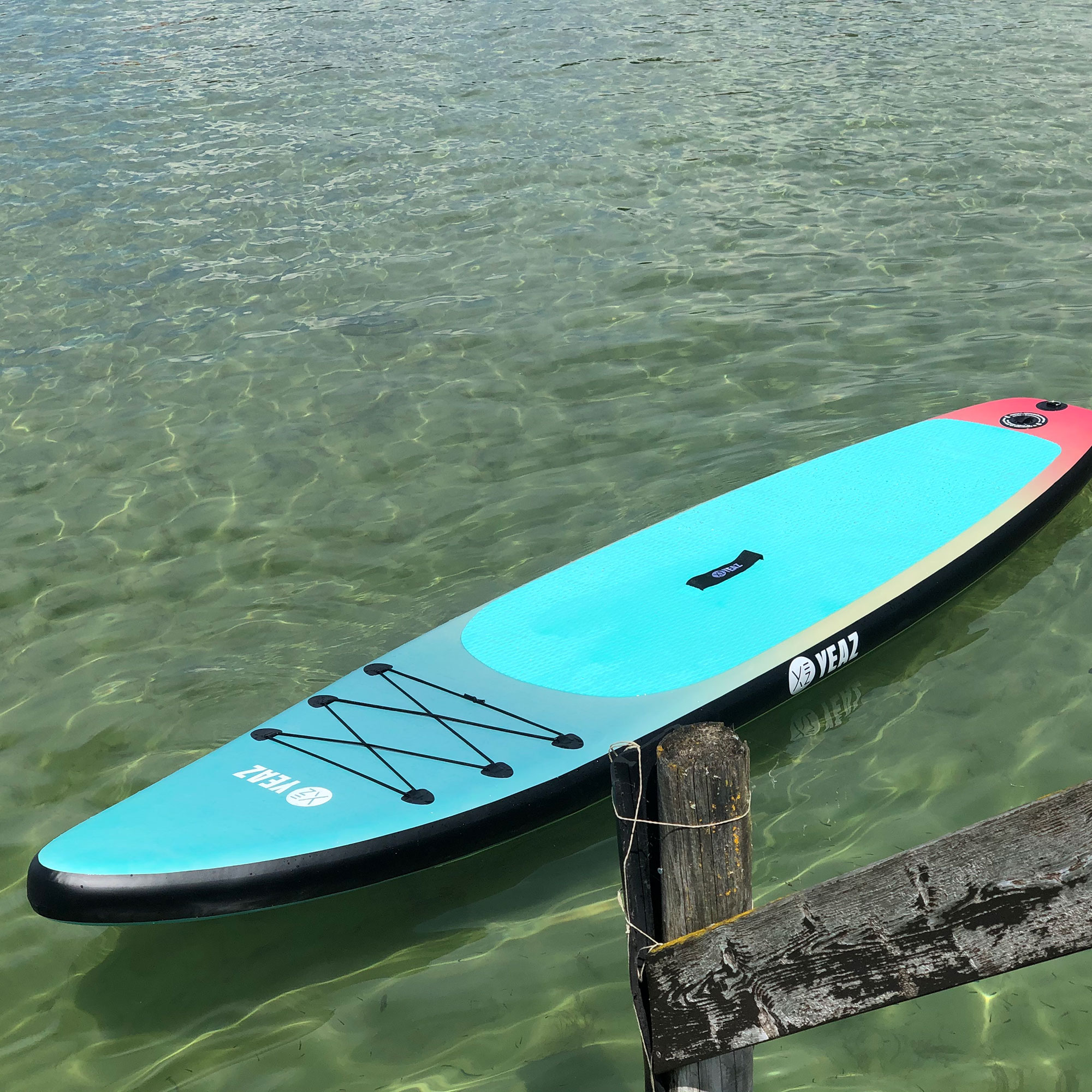Blaues und weißes Paddle-Board auf Wasser. Holzsteg im Vordergrund. Klares Wasser.