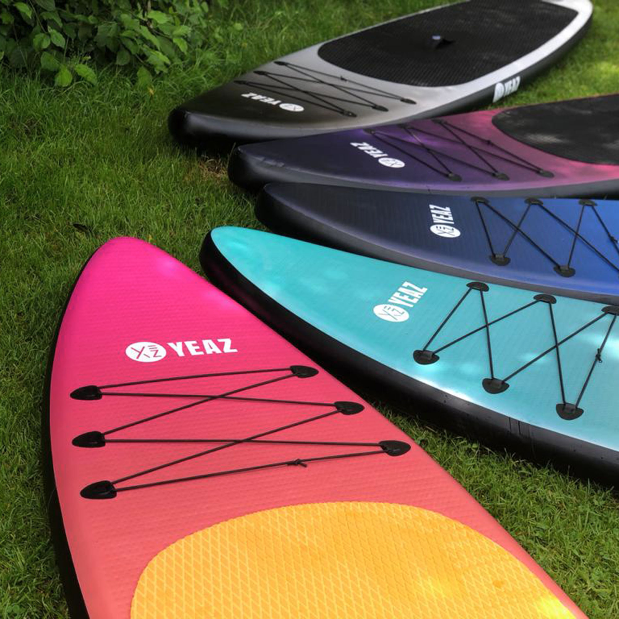 Planches de paddle de différentes couleurs sur l'herbe, avec le mot YEAZ dessus.