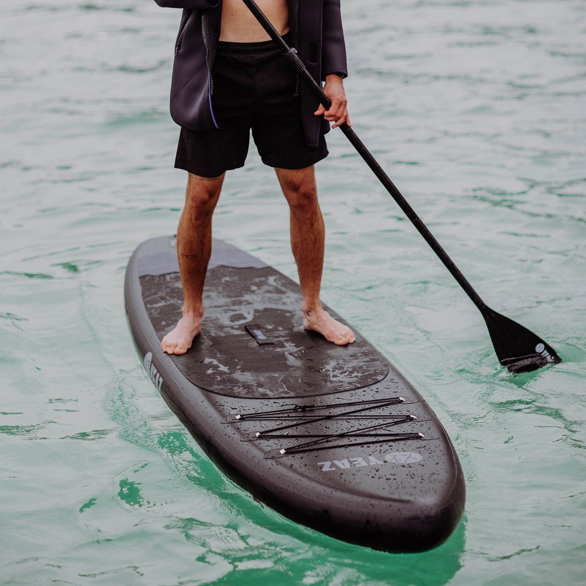 Mann steht auf Paddleboard, hält Paddel, in türkisblauem Wasser.