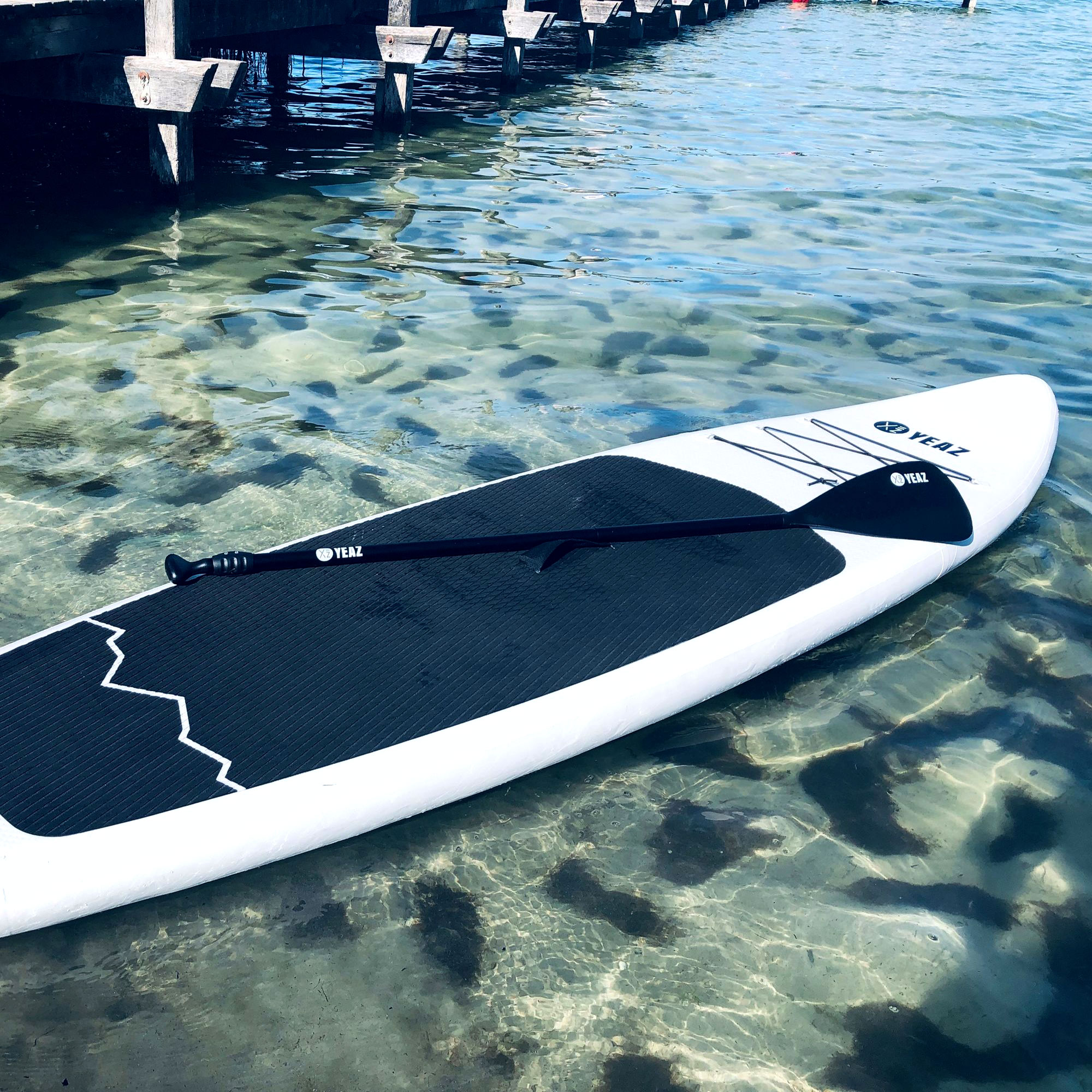 Weißes und schwarzes Paddleboard im klaren Wasser. Ein Paddel liegt auf dem Board.