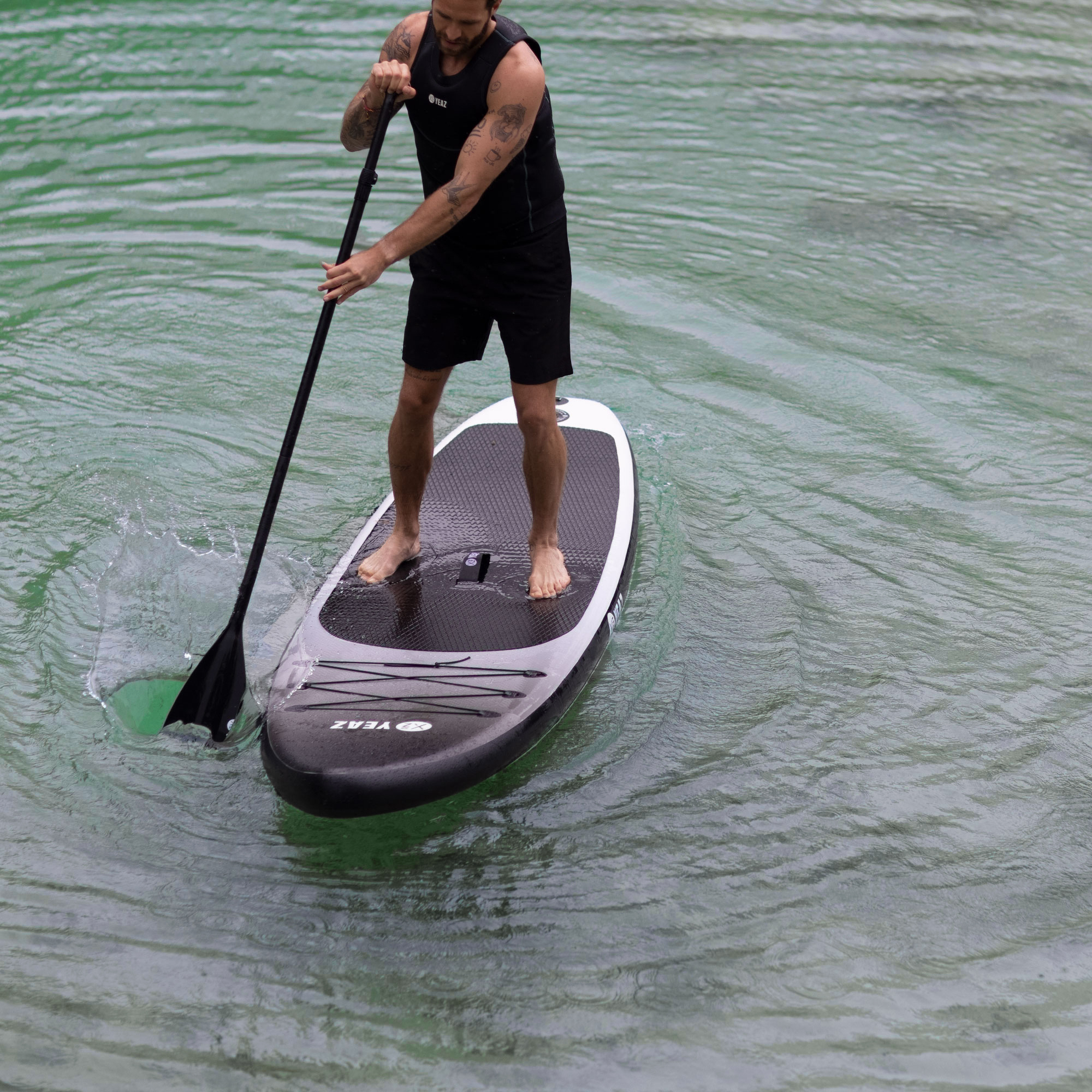 Mann beim Paddeln auf dem Wasser, trägt schwarze Shorts, mit schwarzem Paddel und Board.