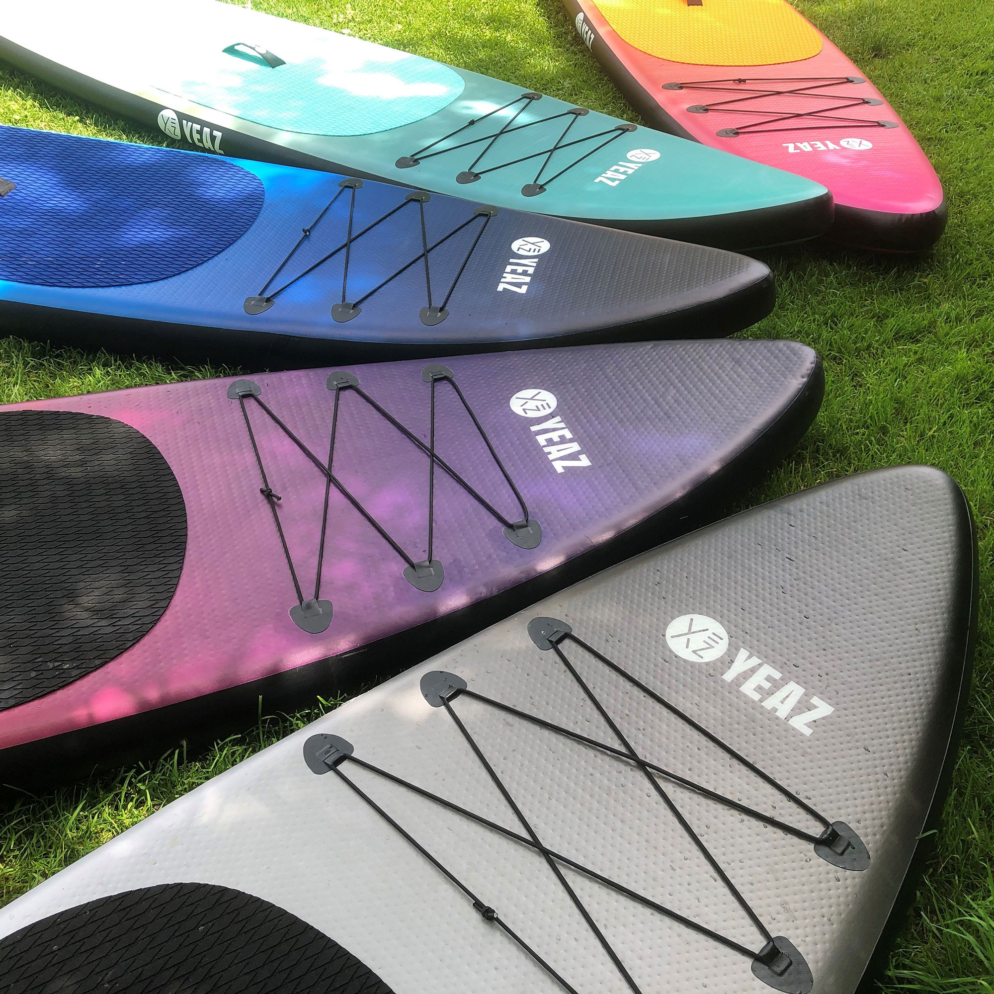 Stand-Up-Paddleboards auf Gras. Mehrere Farben, schwarze Schnüre.