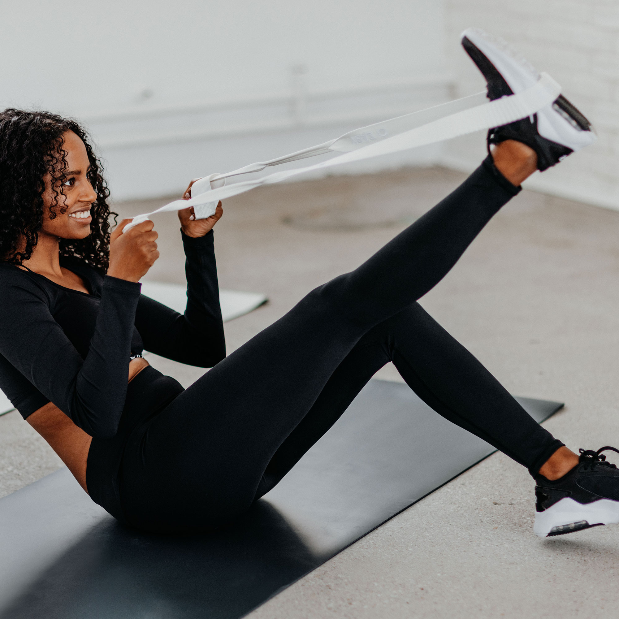 Frau trainiert, dehnt Bein mit Widerstandsband auf einer Matte. Fitnessstudio-Umgebung.