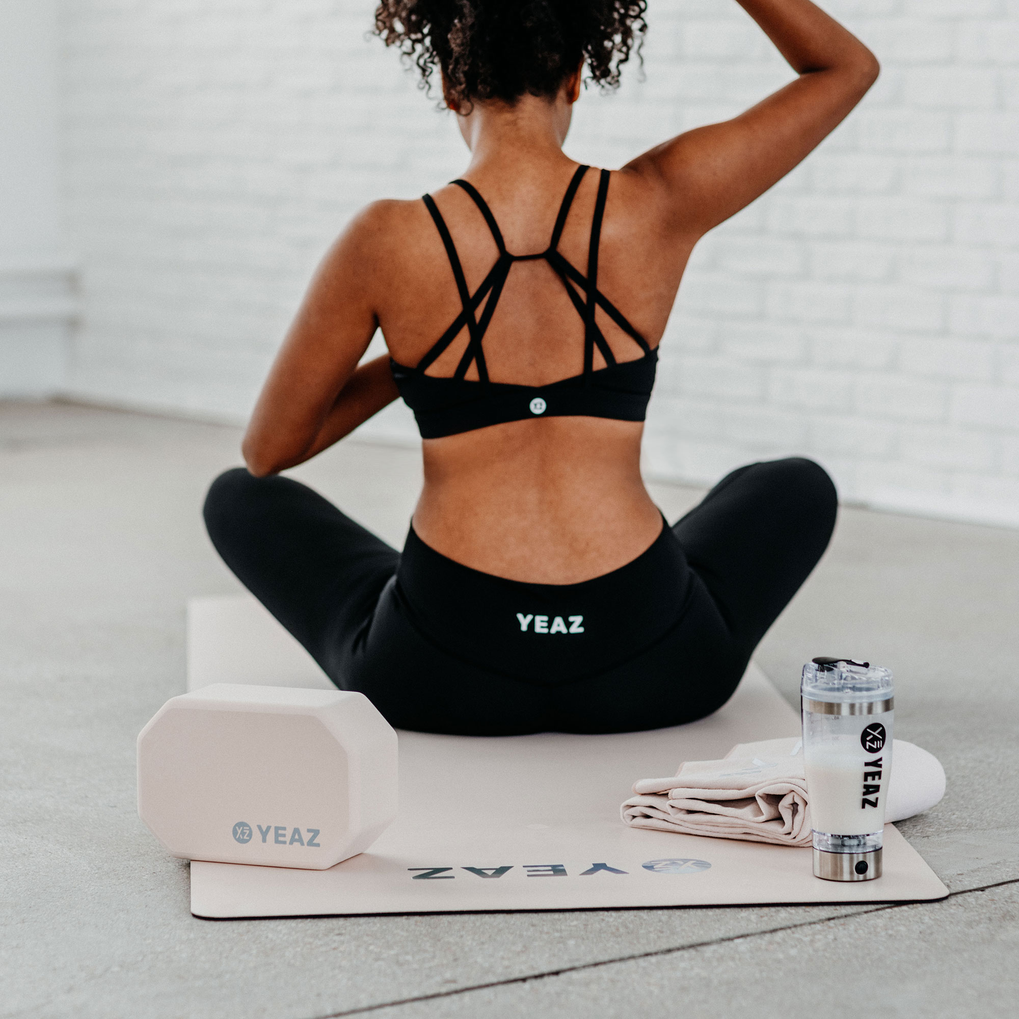 Eine Frau mit Yogamatte, Block, Handtuch und Wasserflasche. Sie ist in einer Yoga-Pose in einem Yoga-Studio.