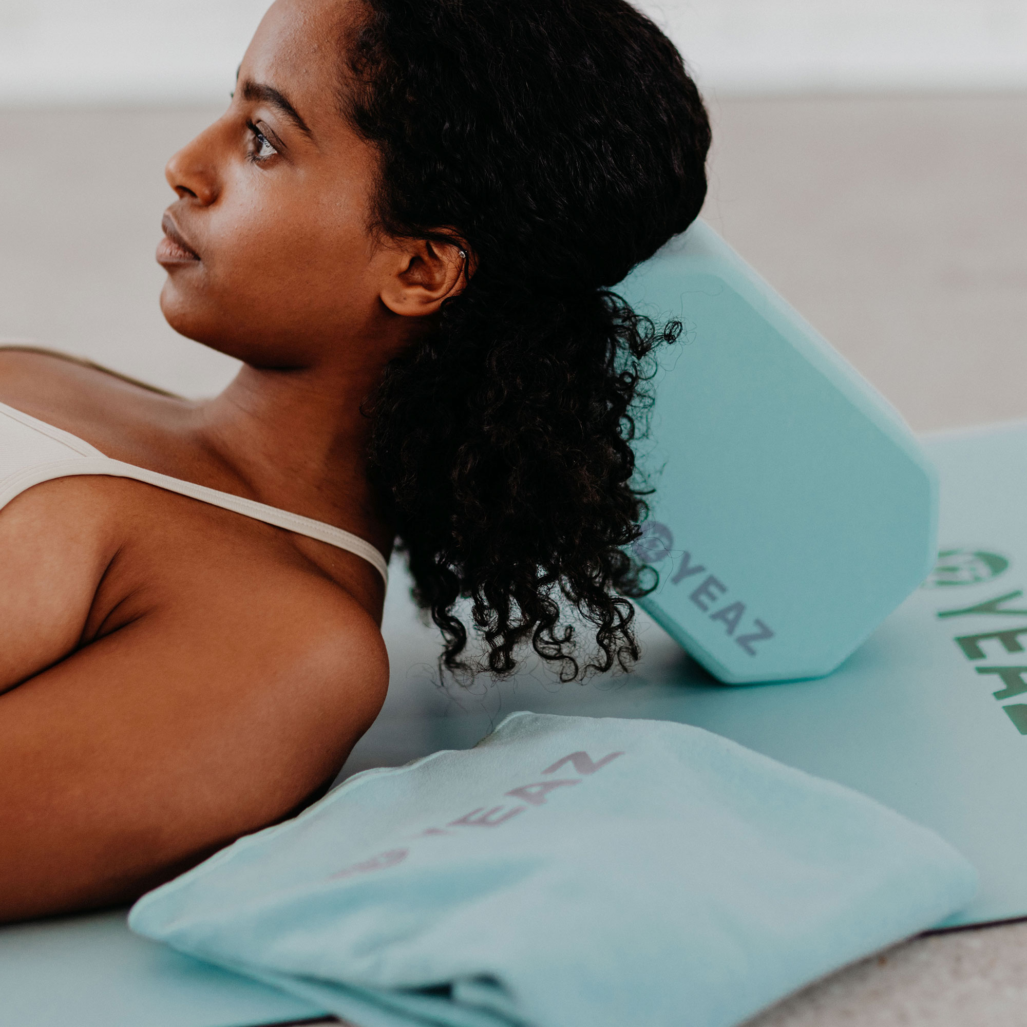 Eine Frau hält einen mintgrünen Yogagurt und blickt nach oben.