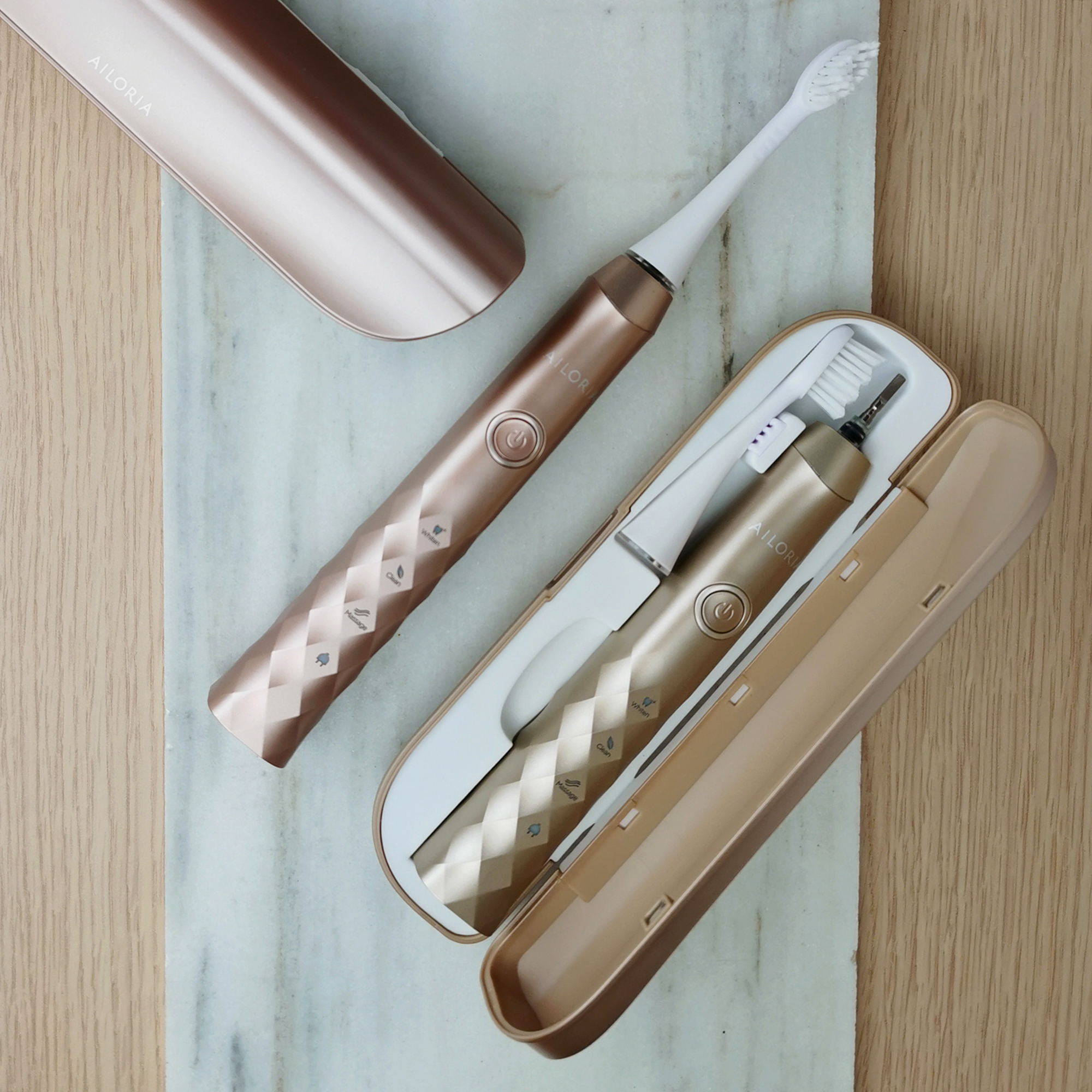 Roségoldene elektrische Zahnbürste und Etui auf Marmoroberfläche neben Holzoberfläche.